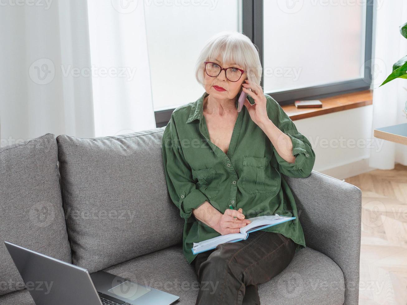 mujer emprendedora senior amigable trabajar desde casa. hablar por teléfono funciona con lap top. negocio, autónomo, concepto de mujer mayor foto