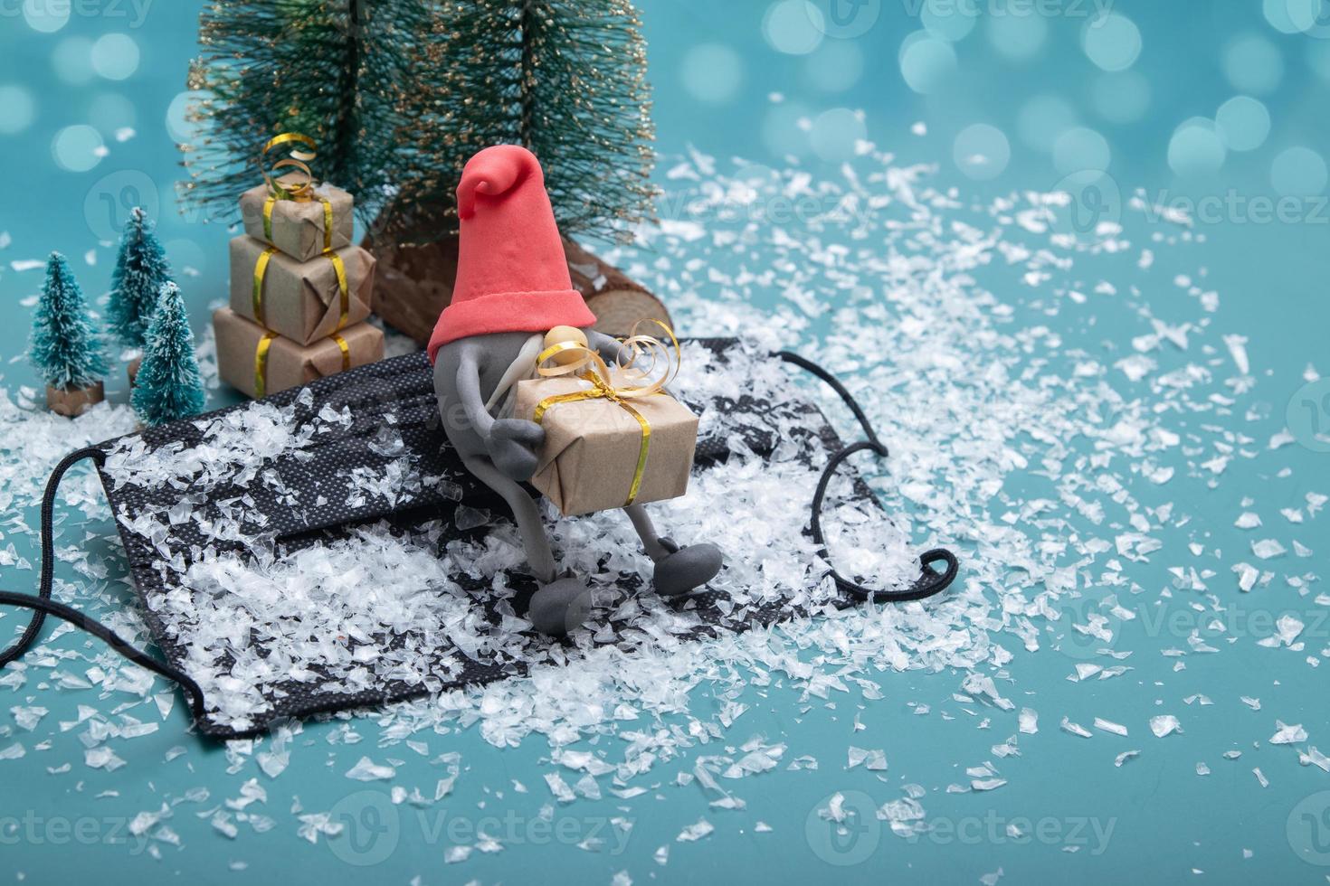 gnomo escandinavo sentado en una máscara médica cubierta de nieve con regalos de navidad foto