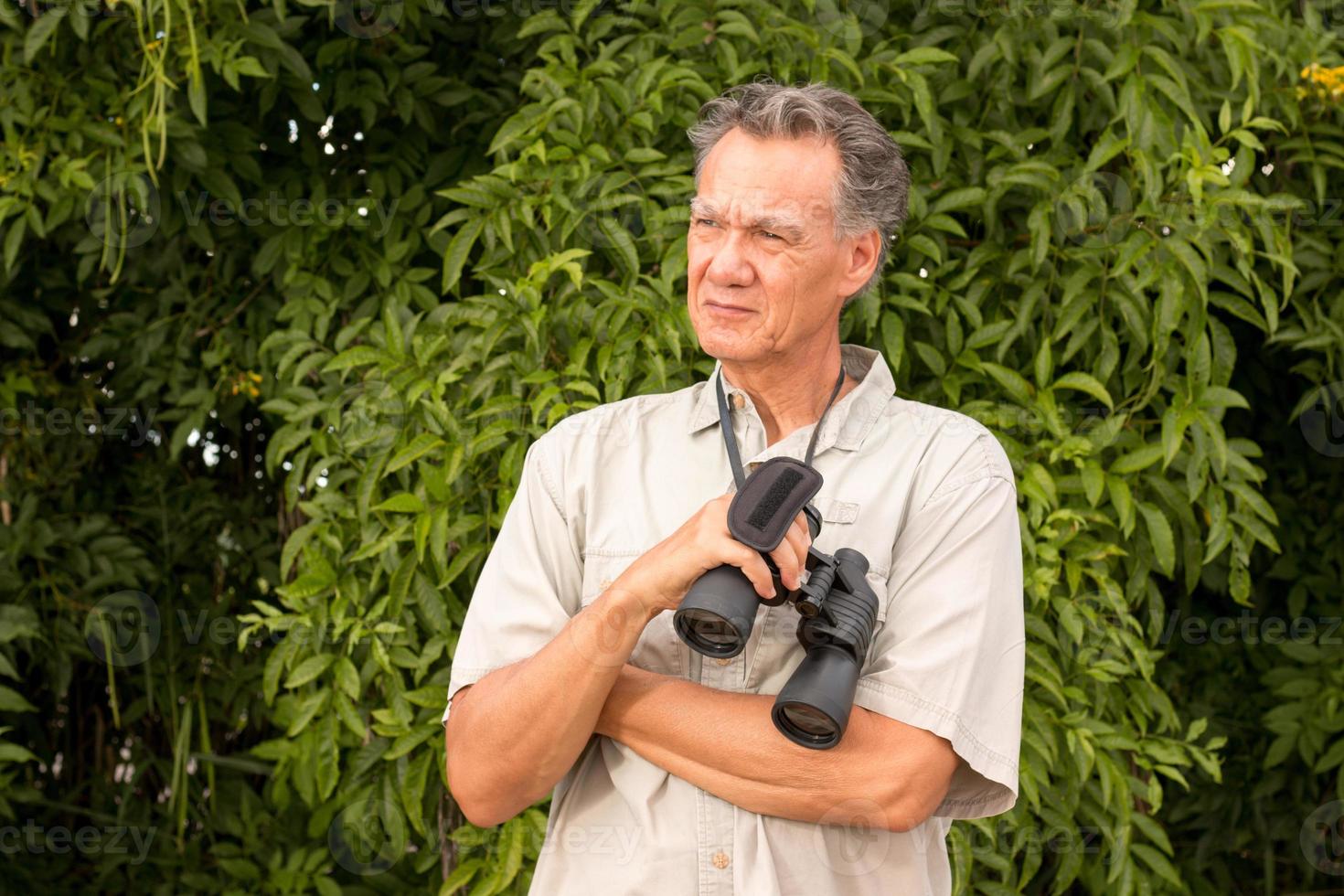 Sesenior hombre maduro fuera de disfrutar de la naturaleza mirando a través de binoculares foto