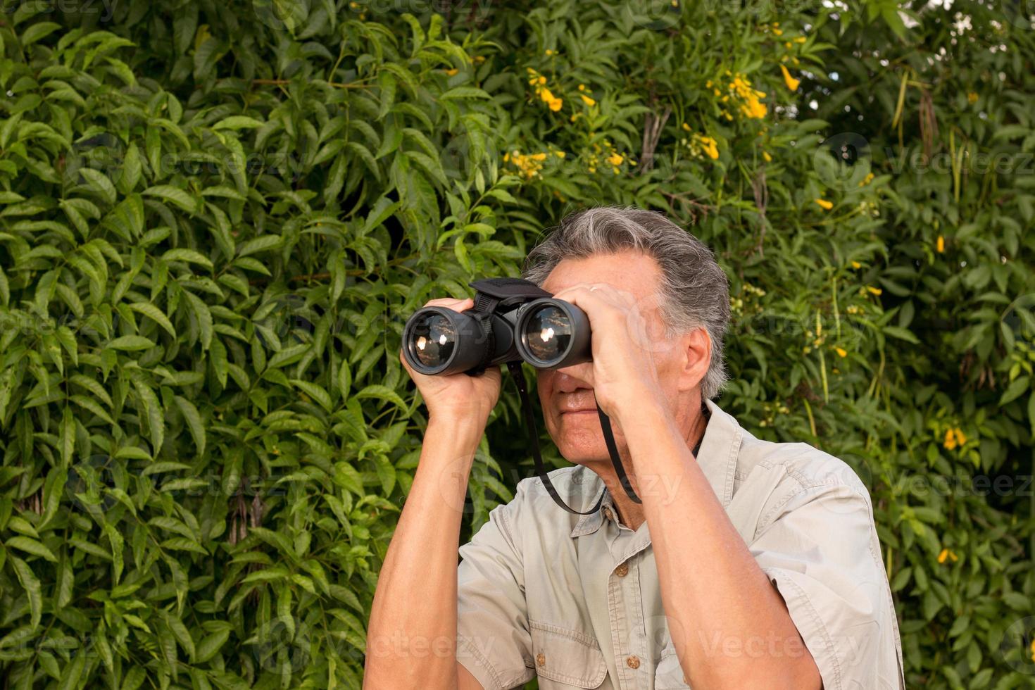 hombre mayor fuera de disfrutar de la naturaleza mirando a través de binoculares foto