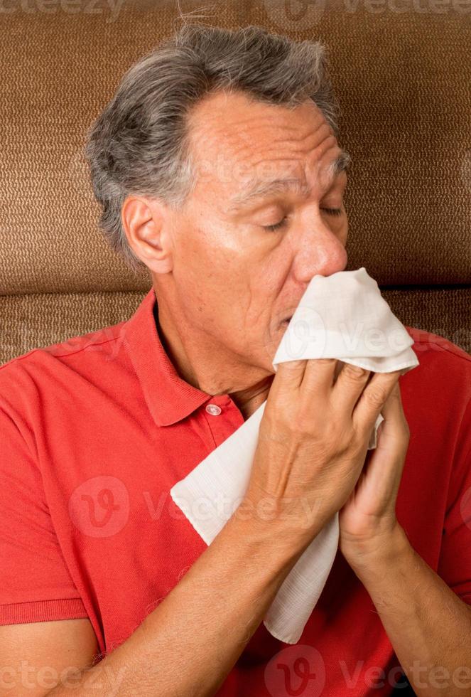 Hombre con gripe estornudando en un pañuelo en su casa foto