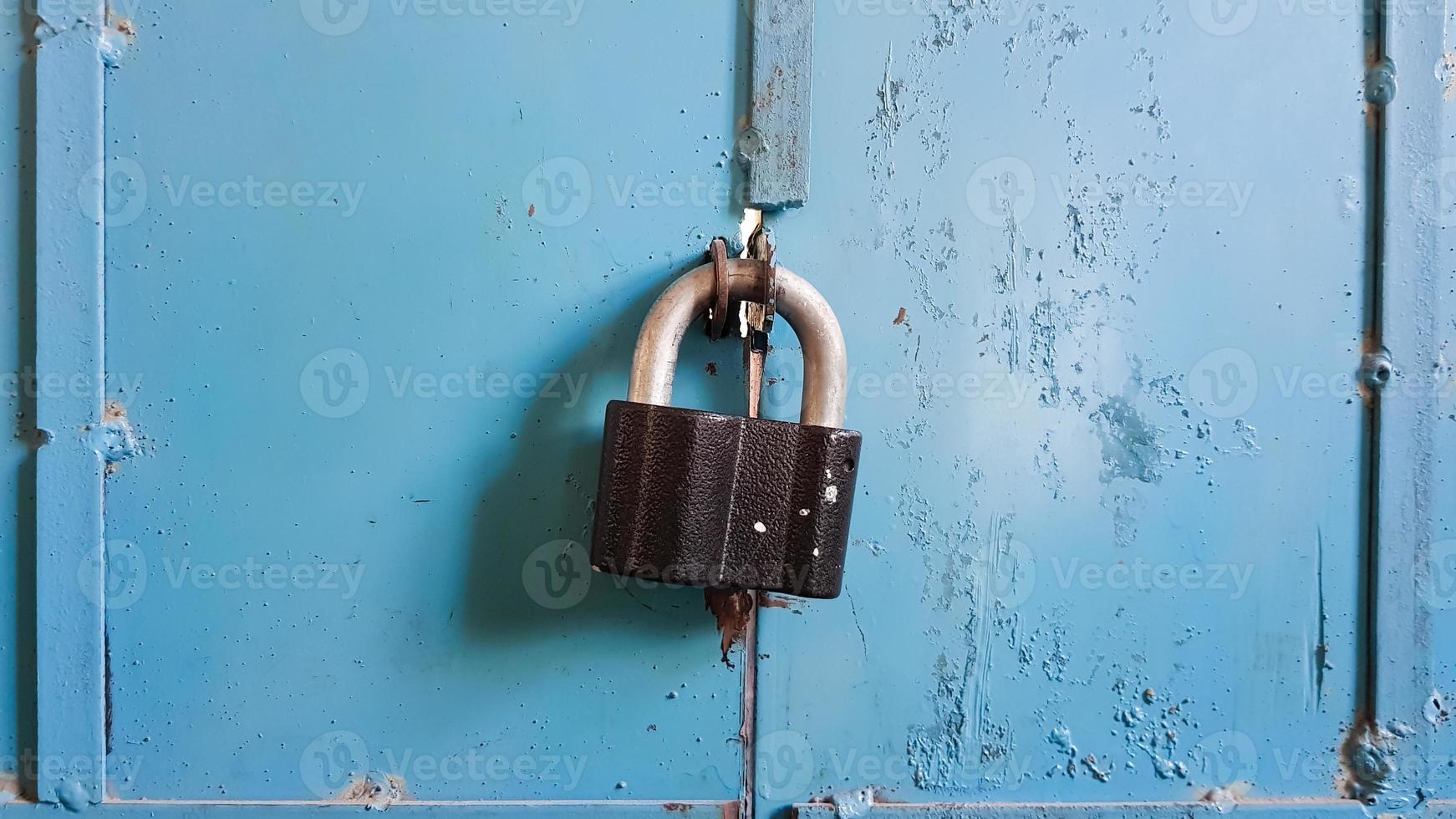 A black padlock on a blue metal garage door. Close-up. photo