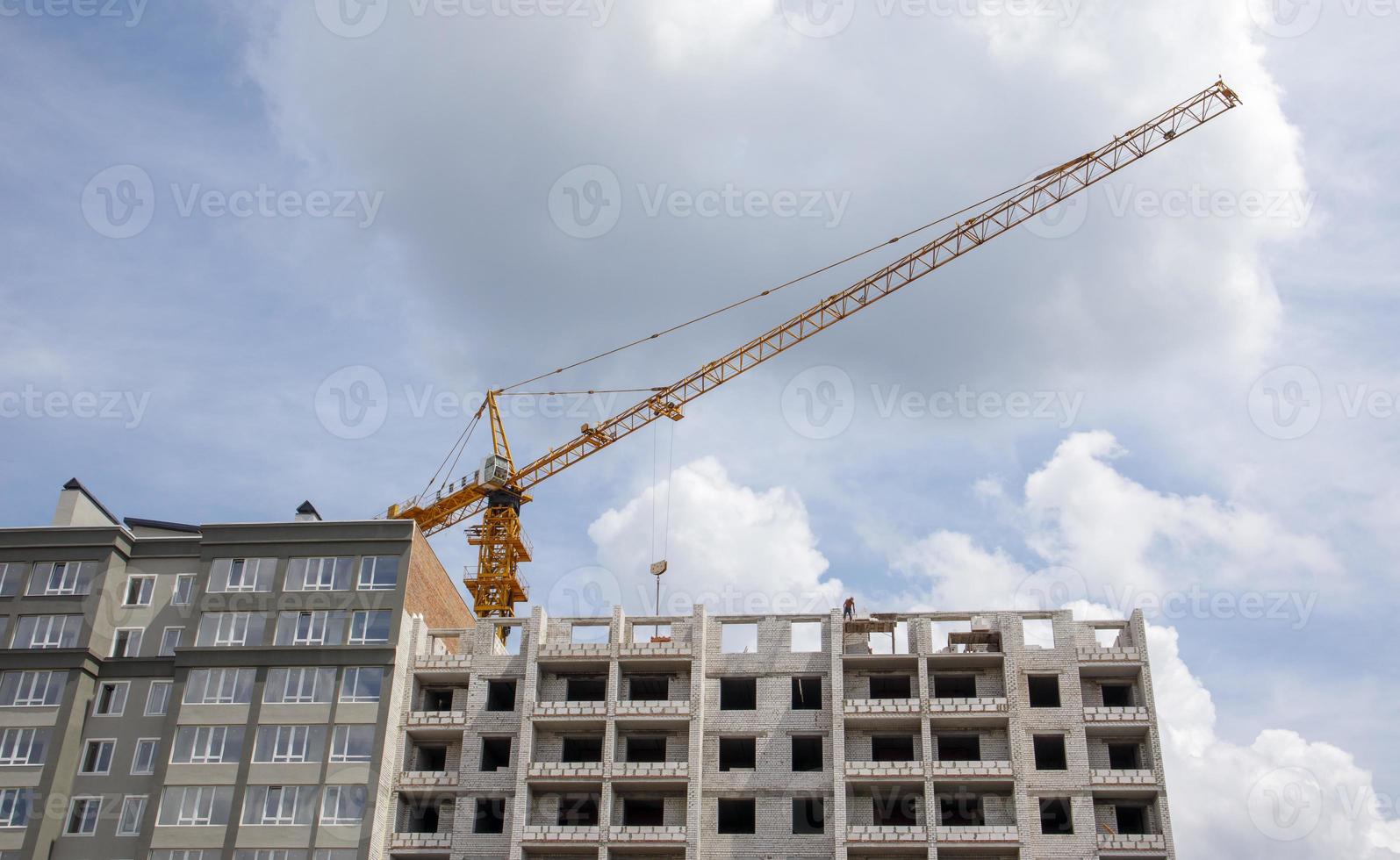 Construction crane on an unfinished residential building against the sun and blue sky. Housing construction, apartment building in the city. Construction site of residential buildings. photo