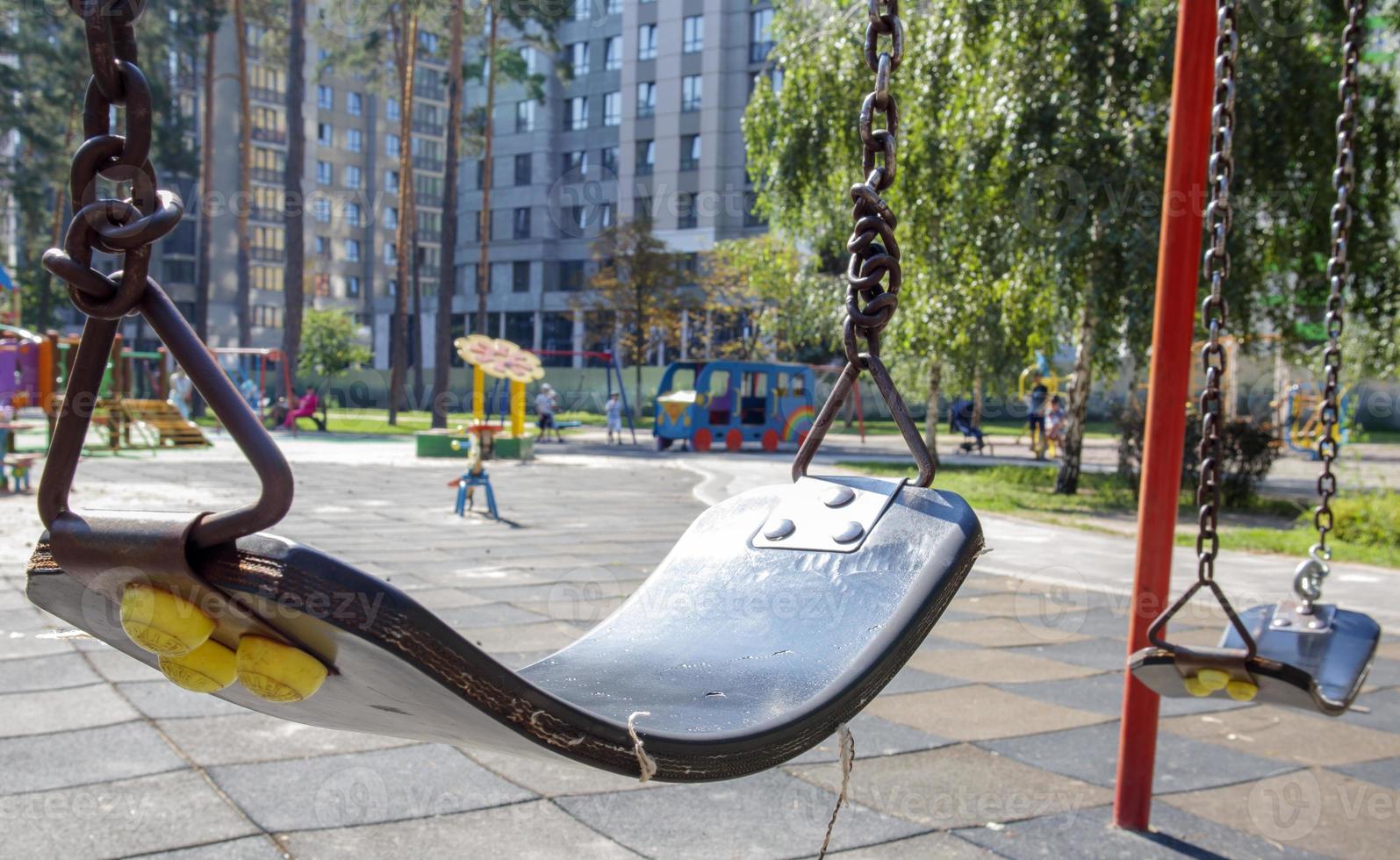 Close up empty baby swing in the park. New chain swing. Set of black swing chains on a modern playground. Focus on the swing in the blurry background. photo