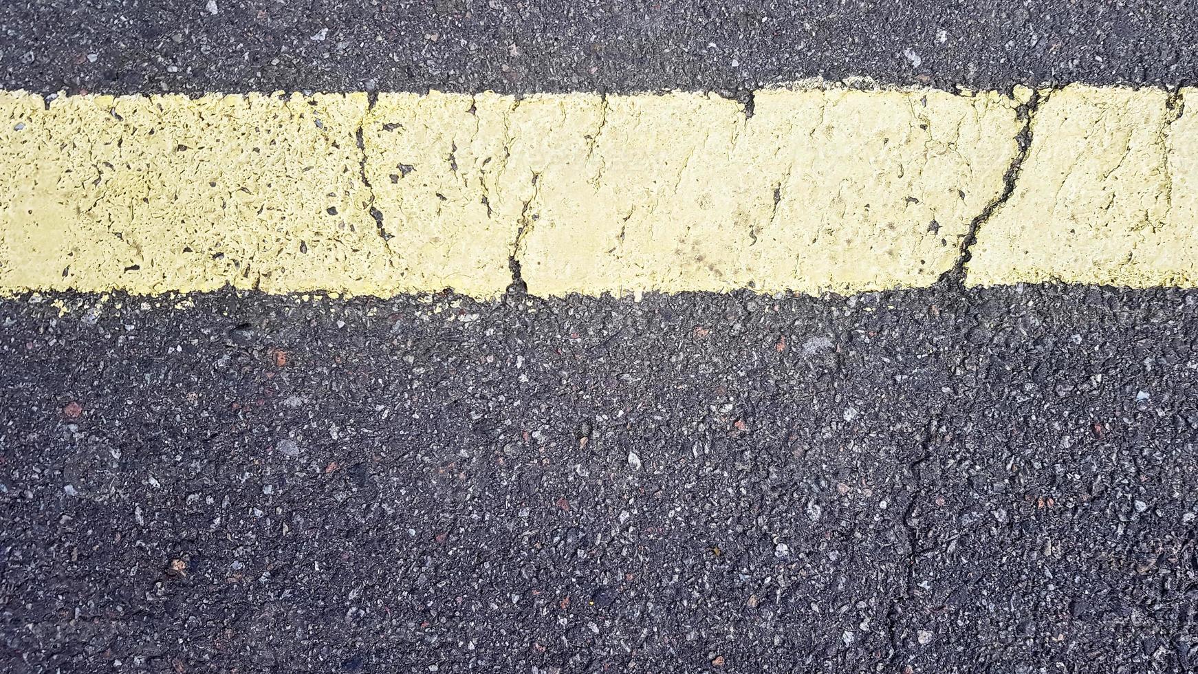 franja horizontal amarilla sobre asfalto. Detalle de una raya amarilla desgastada por el tiempo con una grieta, señalización vial sobre asfalto. foto