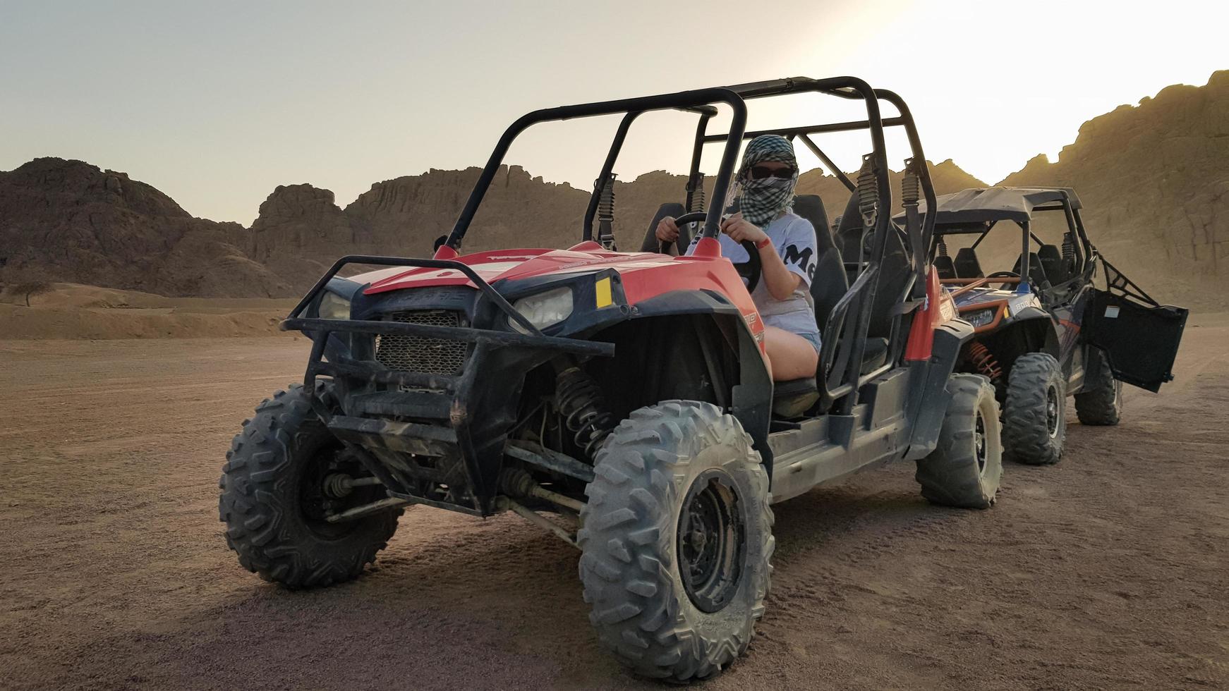 egipto, sharm el sheikh - 10 de octubre de 2020. mujer activa conduciendo un vehículo todo terreno en un camino de tierra en el desierto con el telón de fondo de montañas rocosas de arena en la puesta de sol. foto