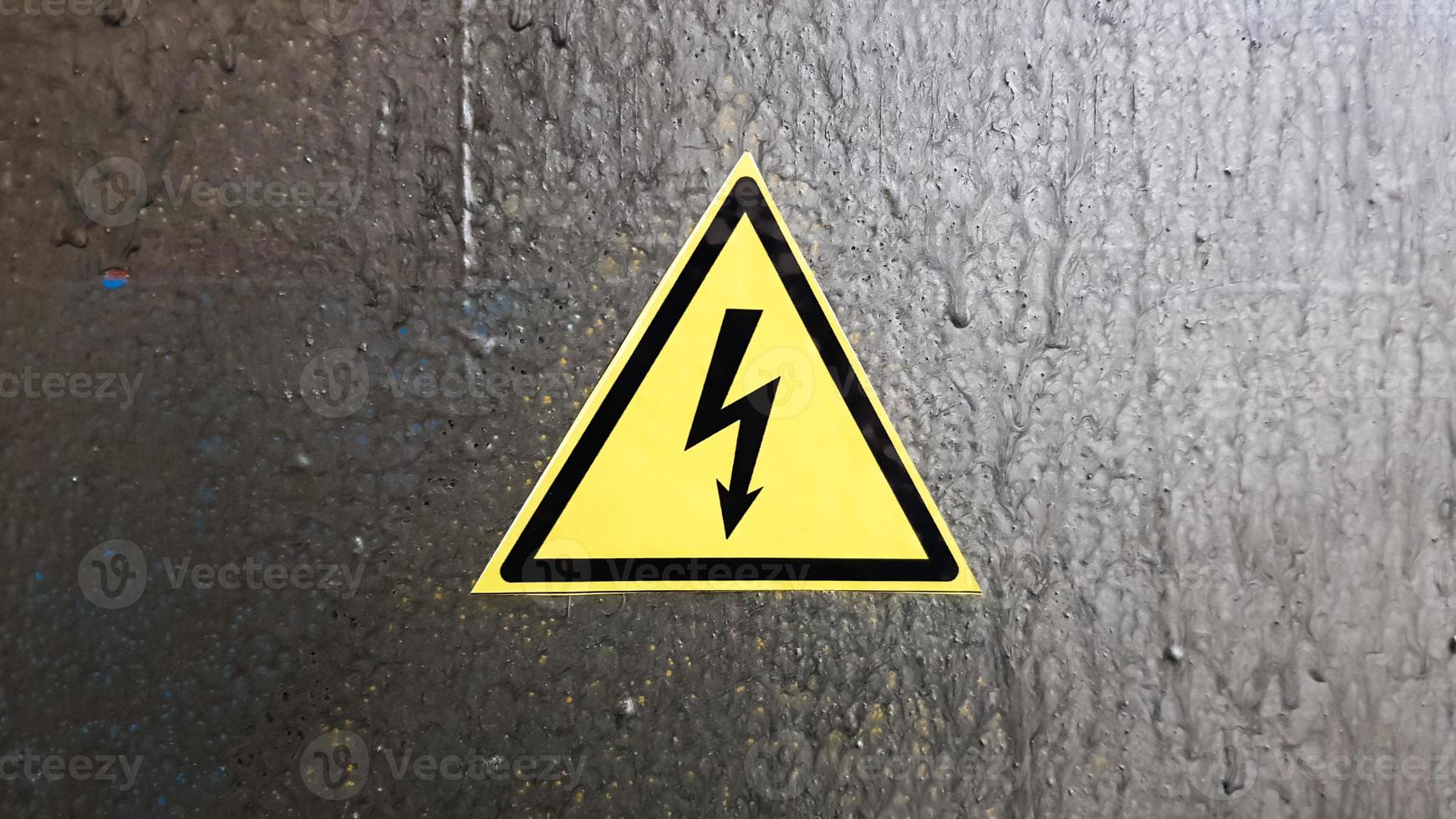 señal de seguridad amarillo y negro sobre un fondo de metal plateado. relámpago de alto voltaje en un triángulo precaución precaución peligro electricidad muerte. foto