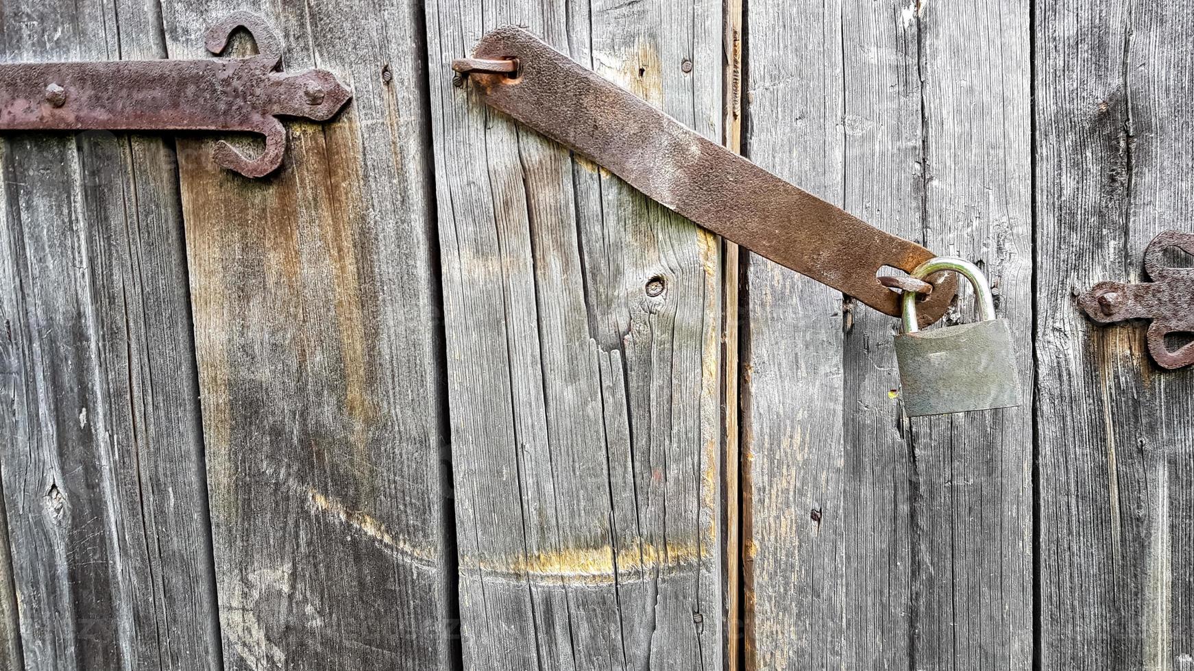 Old vintage metal padlock on a closed wooden door of an old farmhouse. The true style of the village. close-up. focus on the castle. Wooden background, texture. Copy space photo