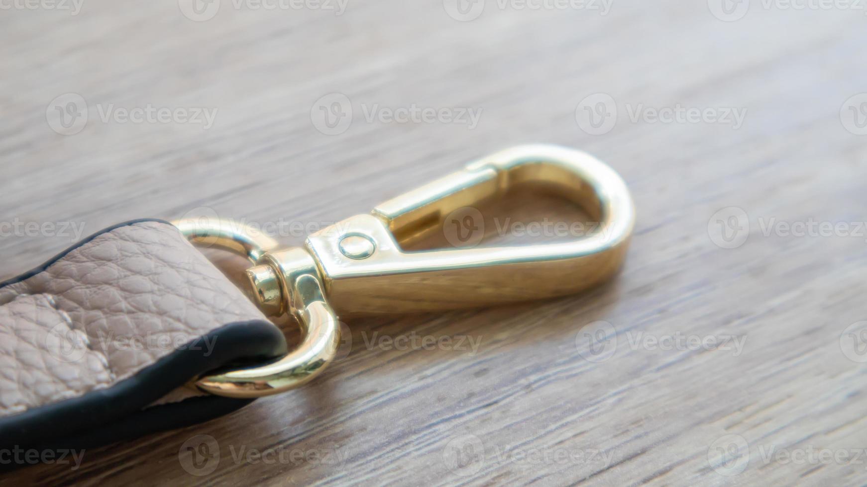 Swivel snap fastener with leather beige bag strap on a wooden background. Metal carabiner with swivel clip or hook. Small gold fittings close-up in selective focus. photo