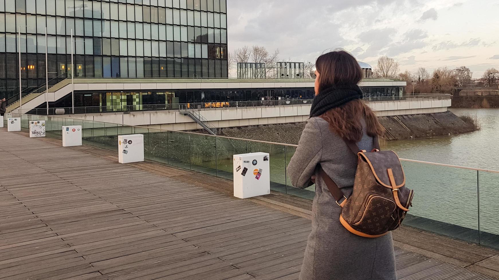 dusseldorf, alemania - 22 de febrero de 2020. una niña con una mochila en un paseo por un puente en el barrio portuario de dusseldorf. eurotrip. turista de la mujer de la visión trasera en el fondo de la arquitectura urbana. foto