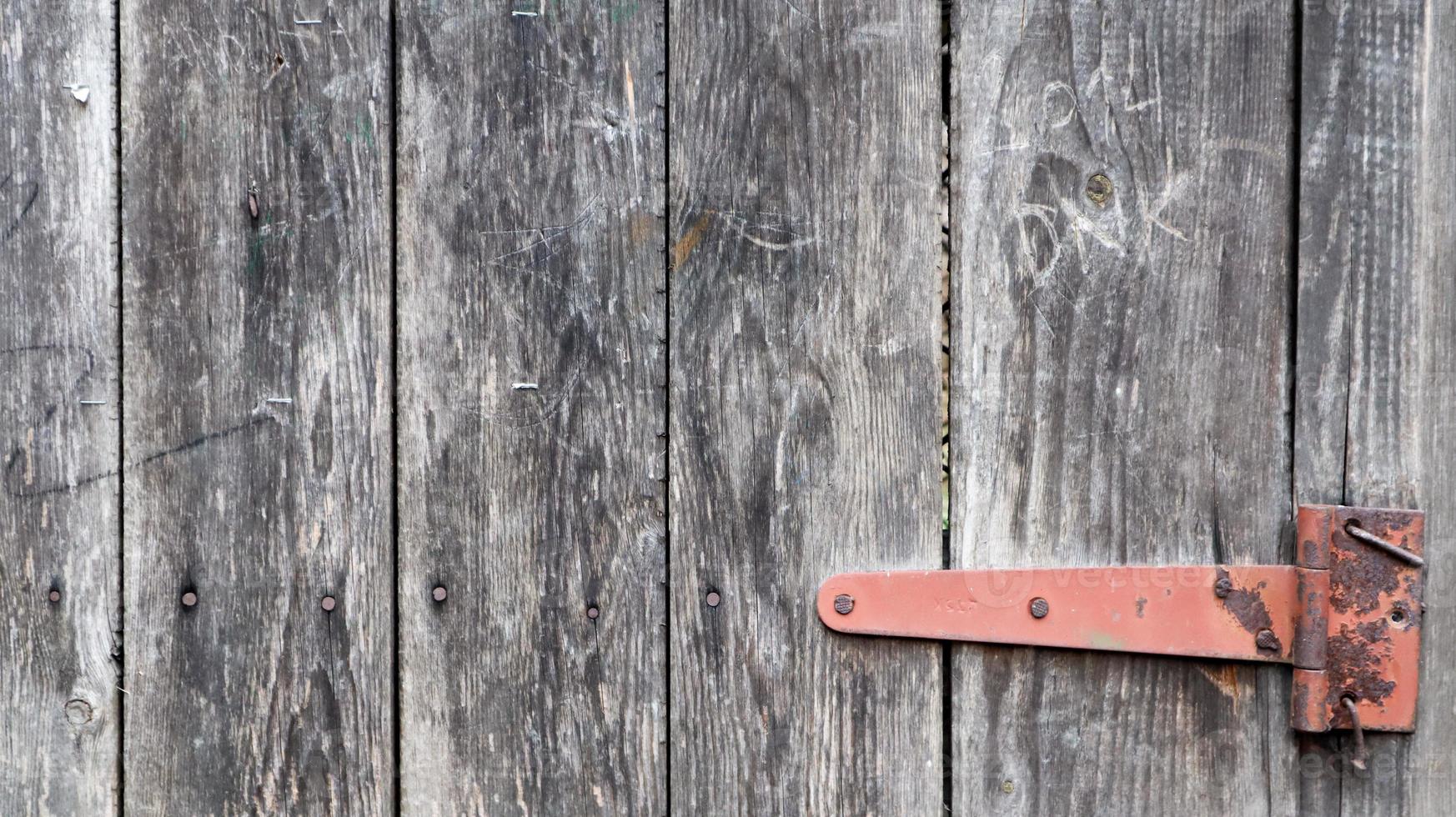 Old wooden background with a rusty hinge. Antique door hinges. Red metal hinge on gray wood close up detailed view. Vintage metal door hinge closeup on old wooden door background. photo