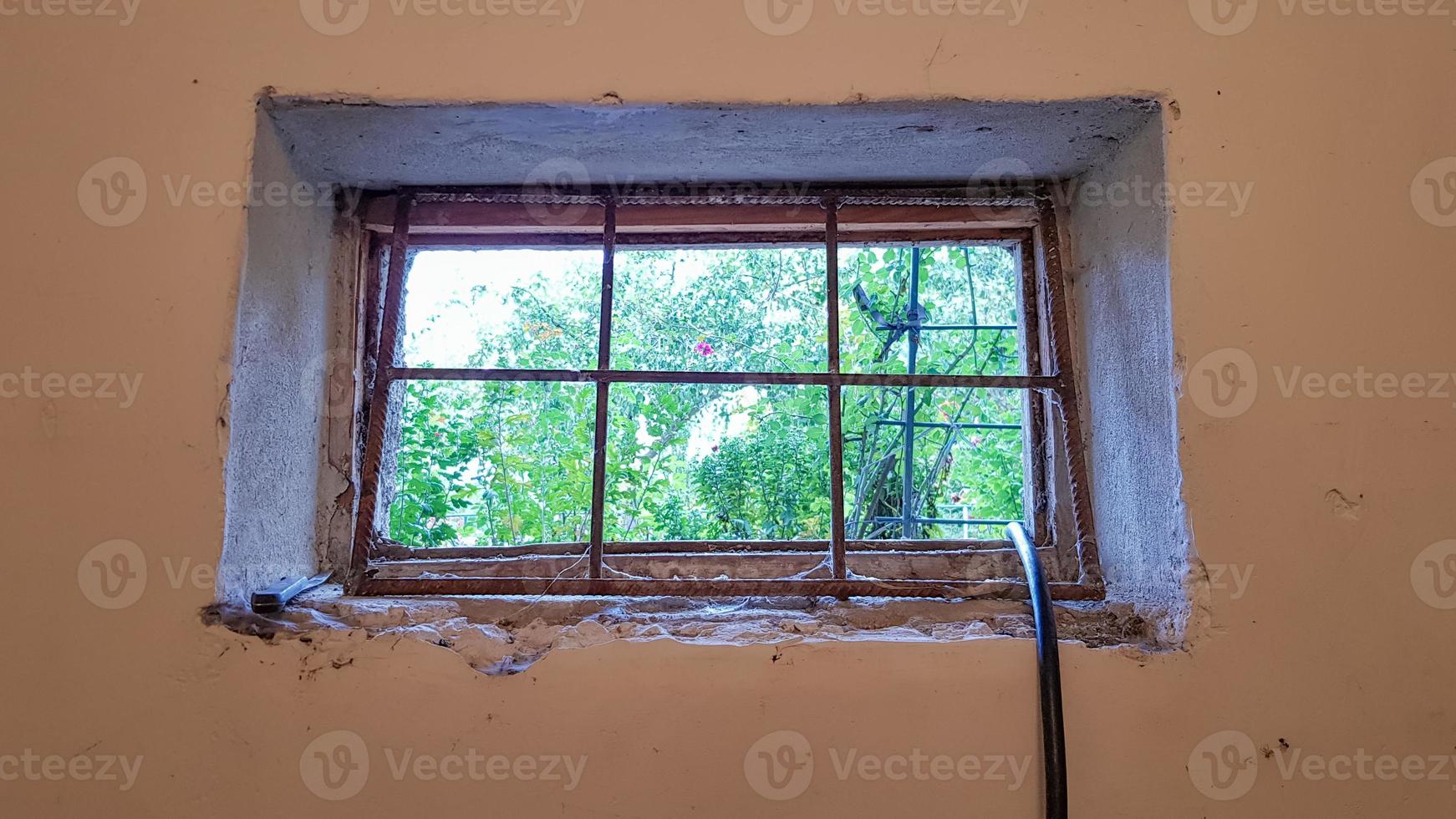 A rectangular basement window is tightened with a metal mesh and a grill. Technical window in the wall of an old gray building. photo