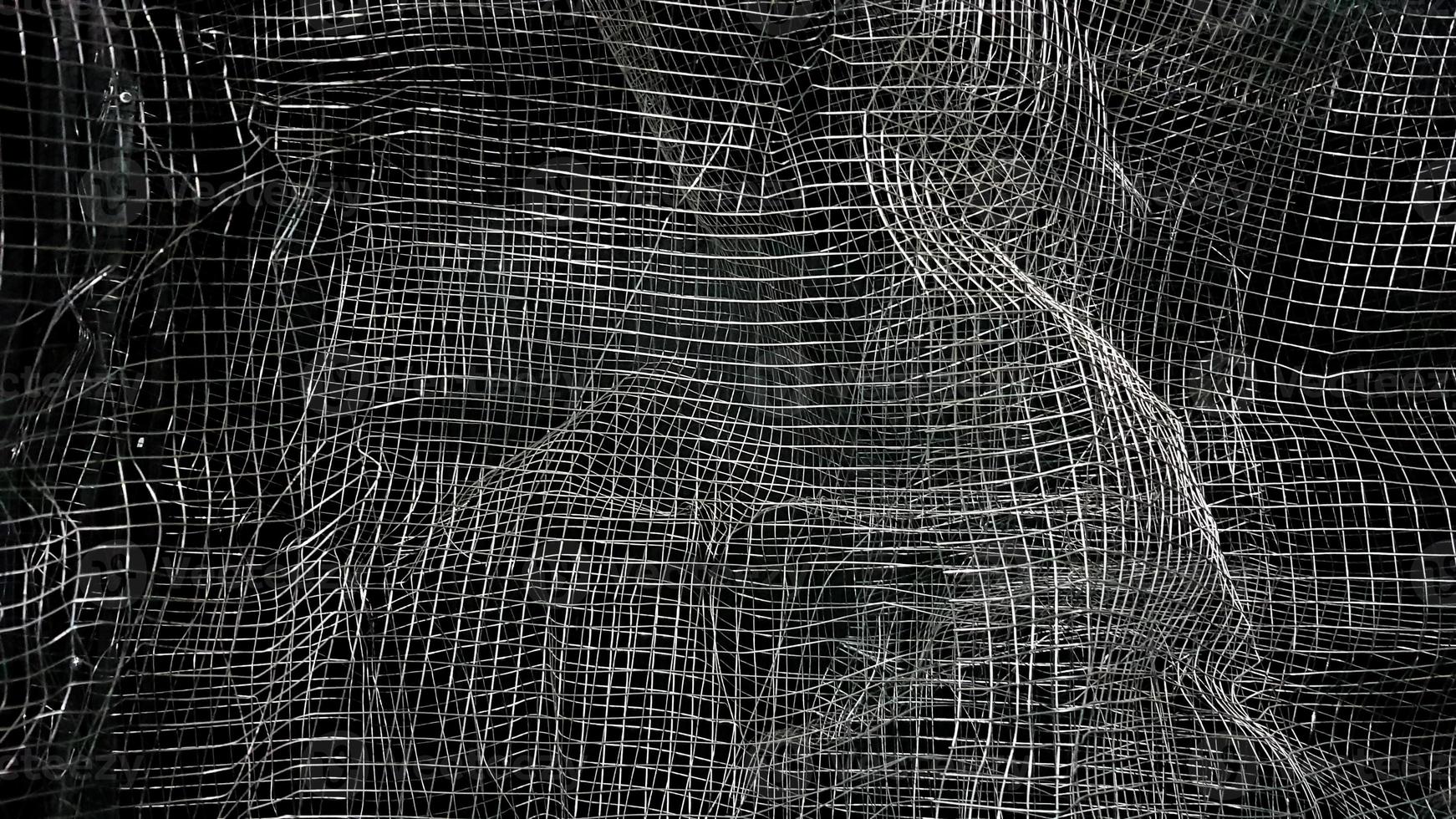 Crumpled mesh. Abstract background. Metal mesh with shadow on a black background. The surface of a large roll is damaged by wire mesh. photo