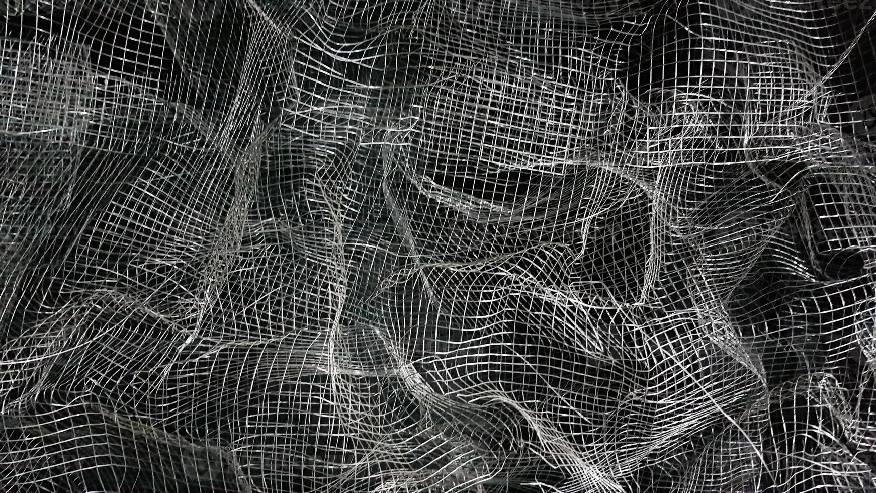 Crumpled mesh. Abstract background. Metal mesh with shadow on a black background. The surface of a large roll is damaged by wire mesh. photo