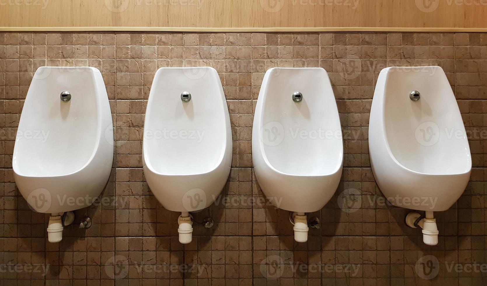 Four urinals lined up on the tiled wall of a modern men's public toilet, no privacy. photo