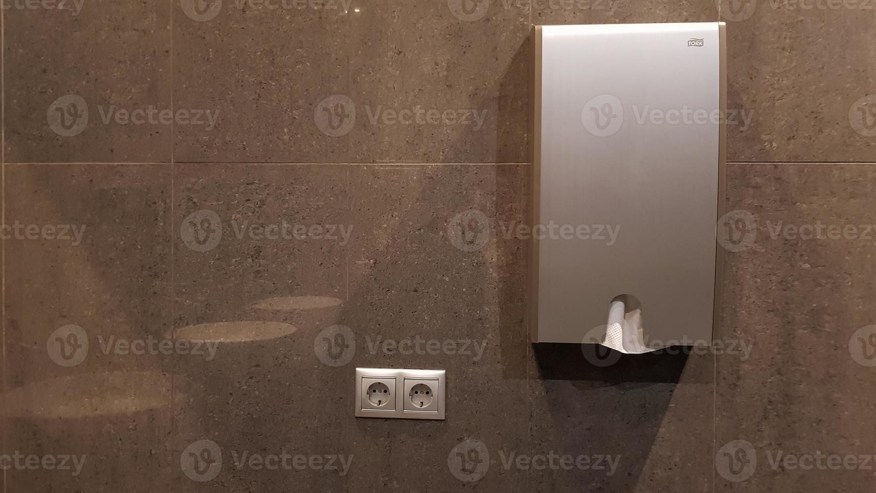 Dispenser or holder for paper towels on a gray tiled wall in a public toilet photo