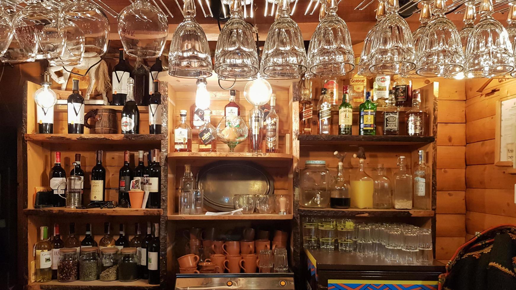 ucrania, kiev - 2 de junio de 2020. copas de vino vacías sobre una barra de madera en un estilo rústico vintage. en el fondo una gran cantidad de diferentes bebidas alcohólicas en botellas de vidrio foto