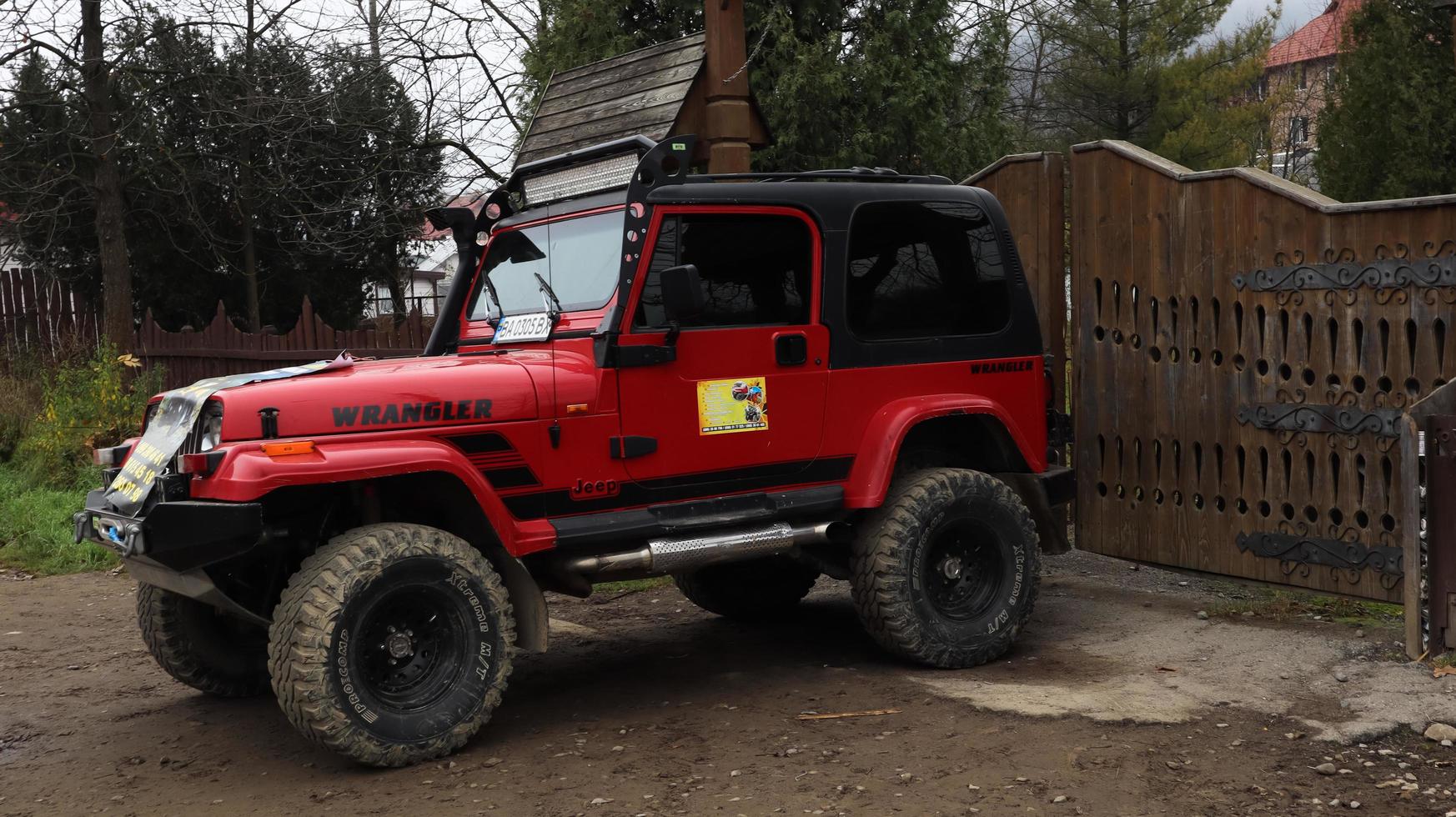 Ucrania, Yaremche - 20 de noviembre de 2019.Un jeep wrangler 4.0i v6 suv rojo está estacionado en una carretera rural cerca de una casa en un pequeño pueblo de los Cárpatos ucranianos. excursiones paseo en jeep de montaña. foto