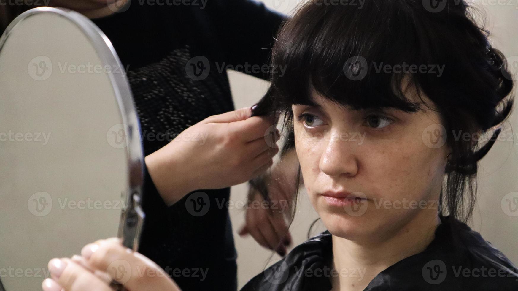 Cerca del maestro peluquero haciendo peinado rizado y maquillaje para mujer hermosa con cabello oscuro en casa. peinado de novia para la novia. foto