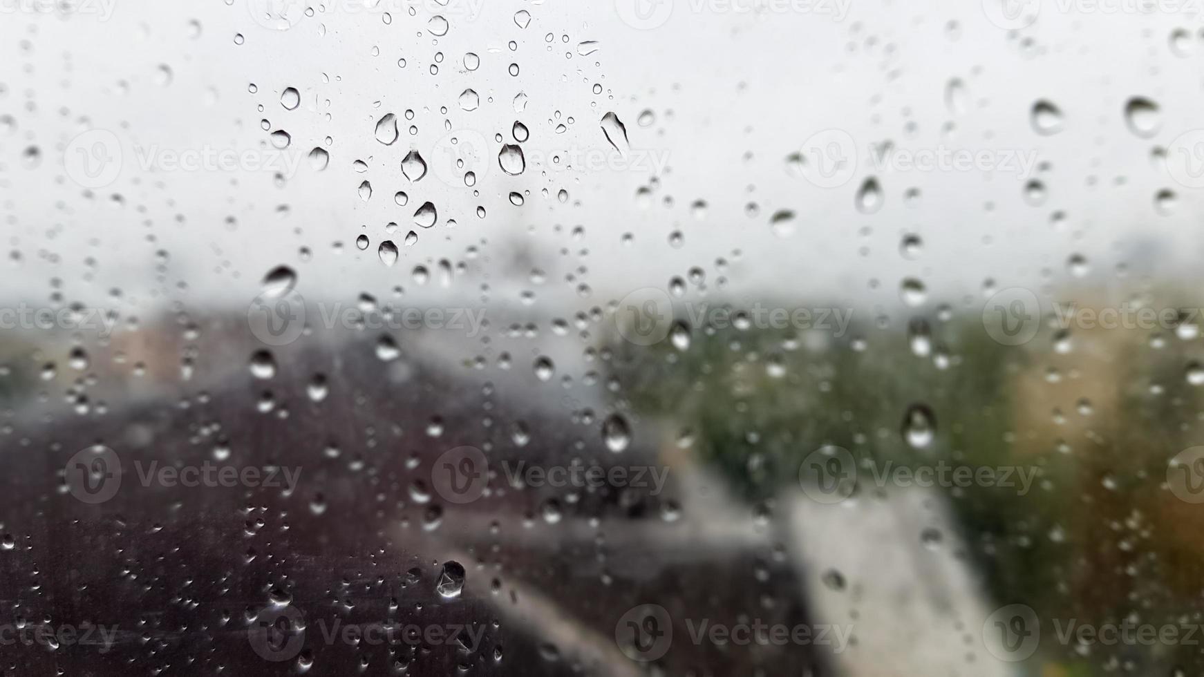 Wet window with drops on the background of the autumn city in cloudy weather. View from the window in the rain. Water drop on glass window during rain with blurred background of city scene photo