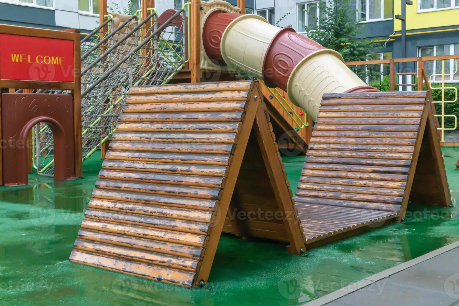 A courtyard of high-rise buildings with a modern and large playground made of wood and plastic on a rainy summer day without people. Empty outdoor playground. A place for children's games and sports. photo