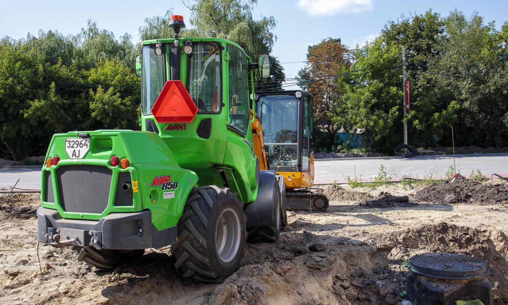 dos pequeñas excavadoras en un gran sitio de construcción. verde brillante en las ruedas y amarillo en las vías. movimiento de tierras y construcción. excavadora de pala. mini cargadores. Ucrania, Kiev - 28 de agosto de 2021. foto