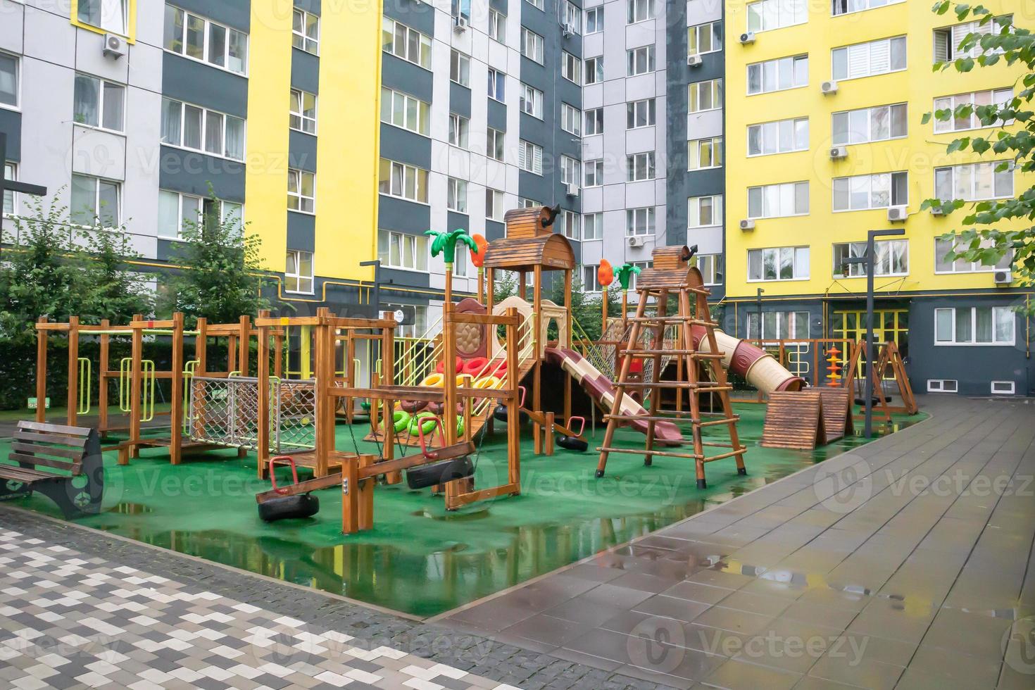 A courtyard of high-rise buildings with a modern and large playground made of wood and plastic on a rainy summer day without people. Empty outdoor playground. A place for children's games and sports. photo