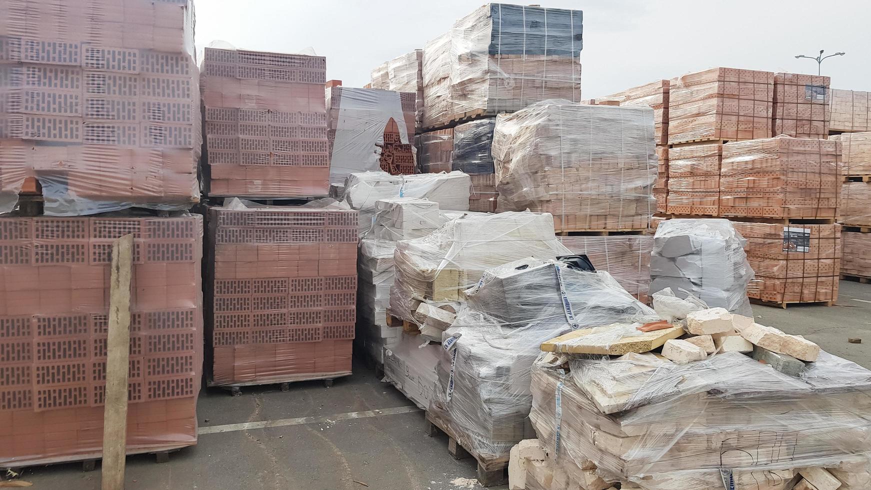 Red perforated bricks with rectangular holes on wooden pallets in an open-air warehouse ready for sale. New bricks on pallets at a hardware store. Ukraine, Kiev - September 6, 2019 photo
