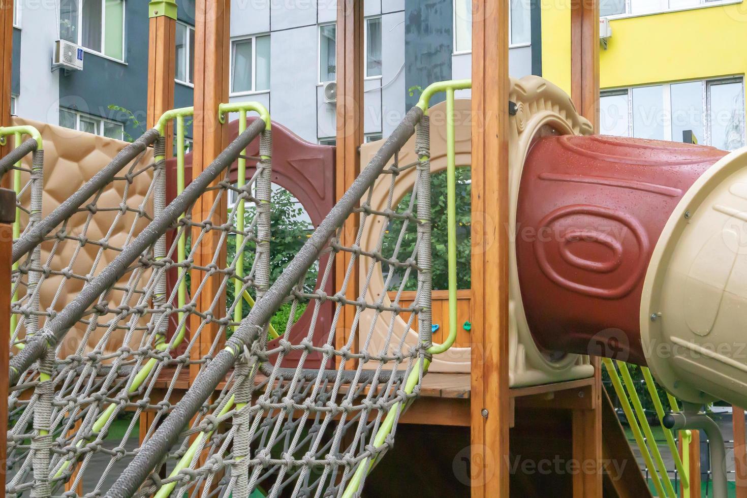 A courtyard of high-rise buildings with a modern and large playground made of wood and plastic on a rainy summer day without people. Empty outdoor playground. A place for children's games and sports. photo