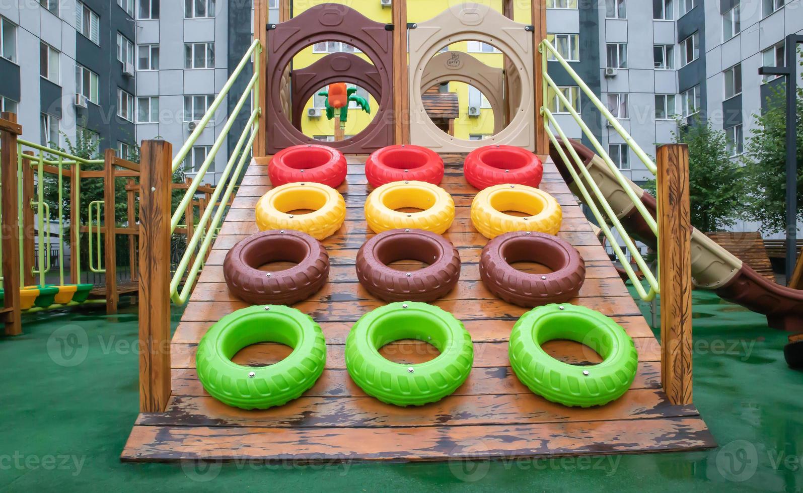 A courtyard of high-rise buildings with a modern and large playground made of wood and plastic on a rainy summer day without people. Empty outdoor playground. A place for children's games and sports. photo