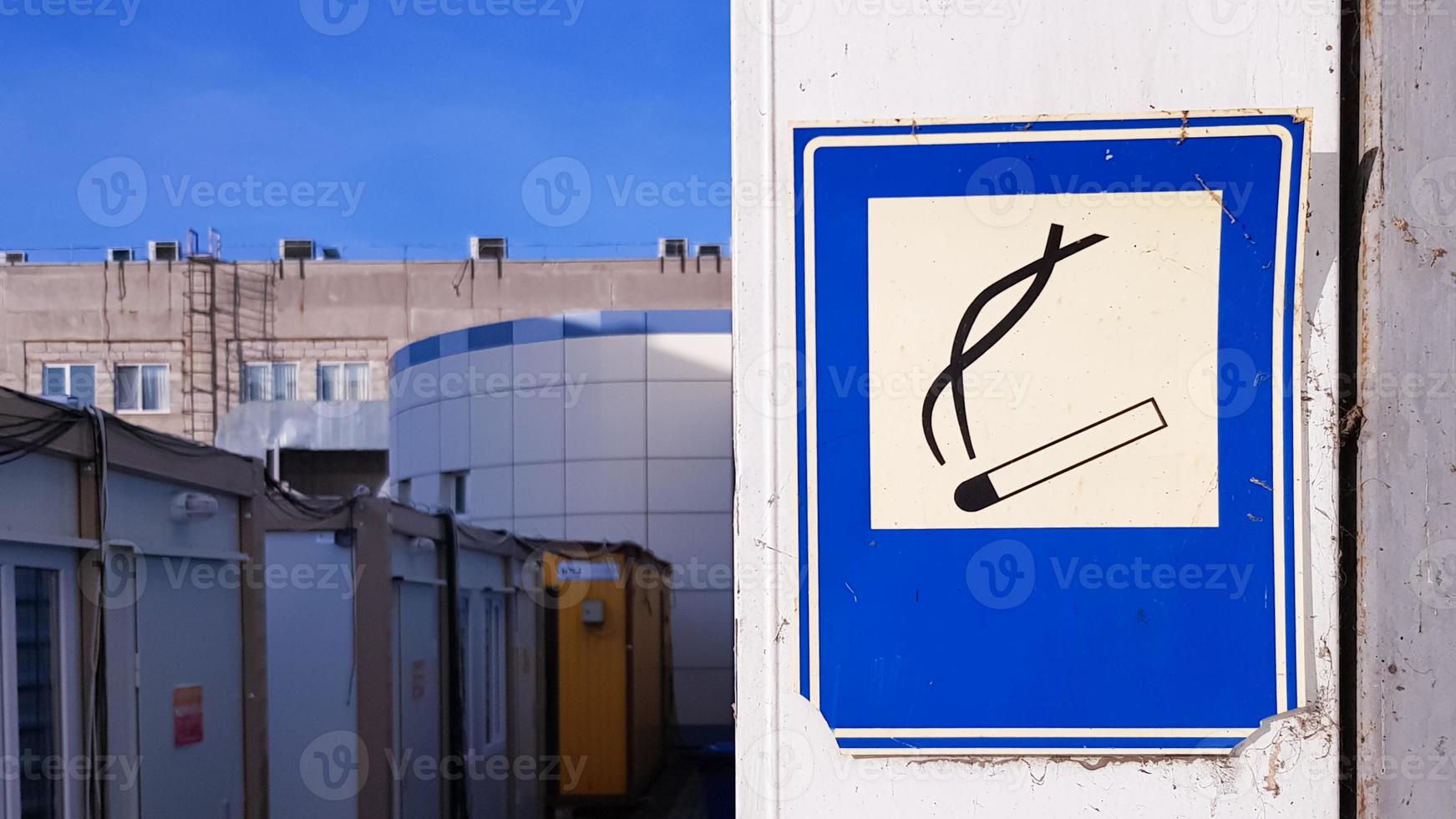 Hay un cartel cuadrado azul pegado en la pared que explica la zona de fumadores en la calle. foto