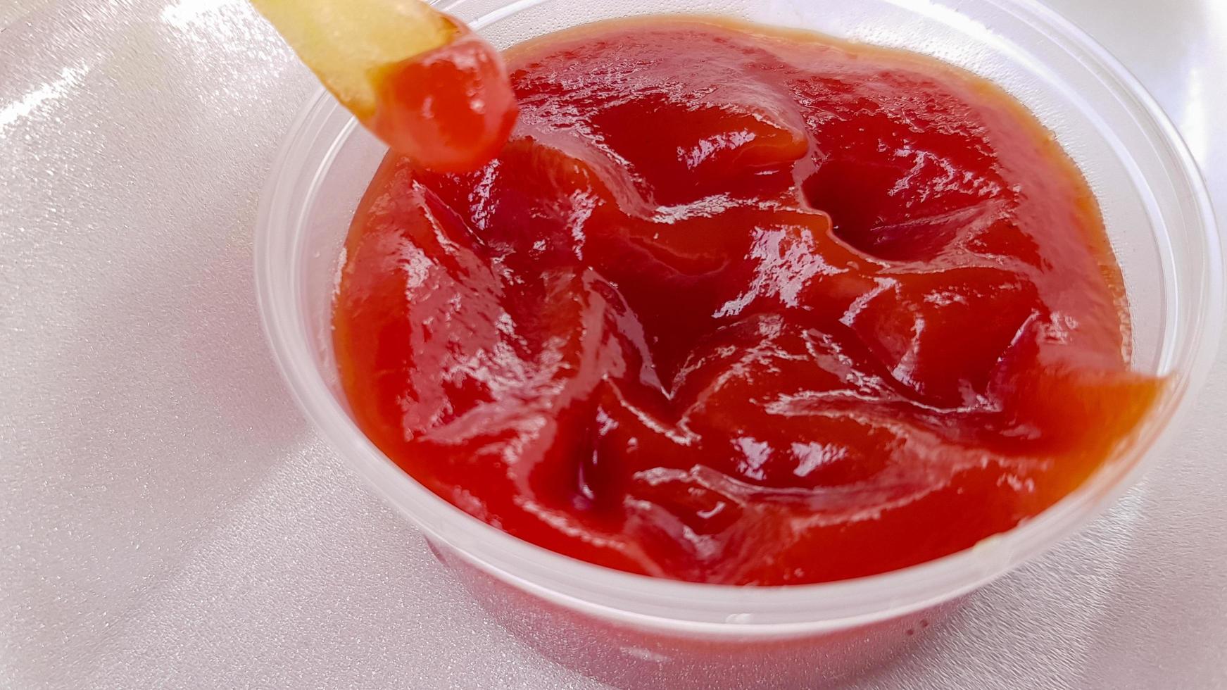 A close-up of golden orange yellow deep fries with tomato ketchup served in a foam container. Fast food takeaway. Unwanted fresh food. photo