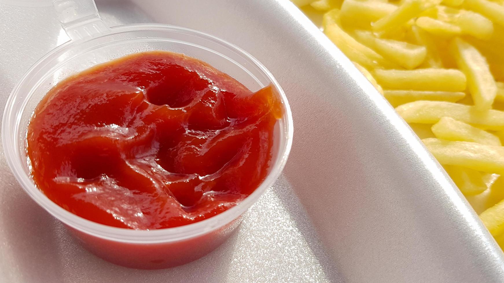 A close-up of golden orange yellow deep fries with tomato ketchup served in a foam container. Fast food takeaway. Unwanted fresh food. photo