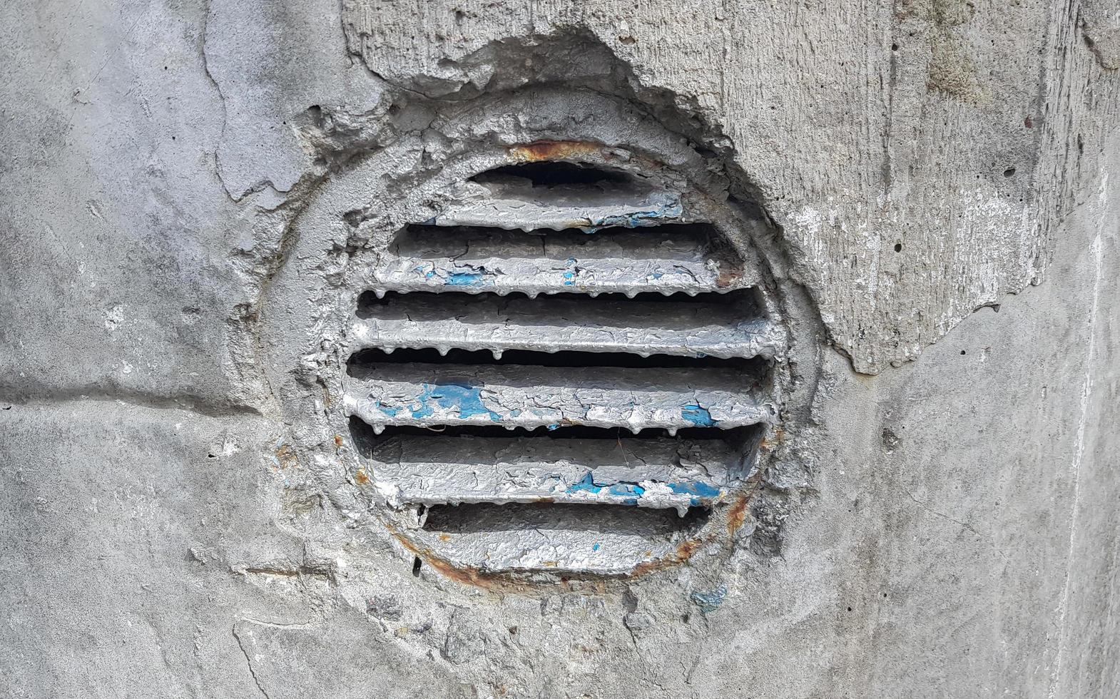 ventilation hole in concrete. Metal industrial round ventilation cover. Rusty and dirty old round ventilation frame with horizontal metal stripes. photo