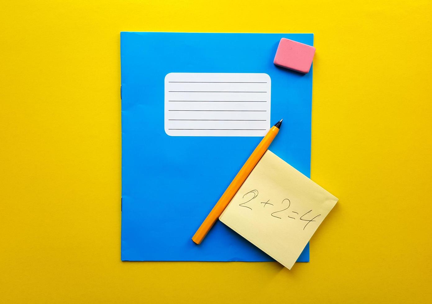 Blue notebook and textbook copy butt for school subjects, eraser, pencil, paper clip on a yellow background. The solution to the mathematical problem is written in pencil. Flat lay, copy space photo