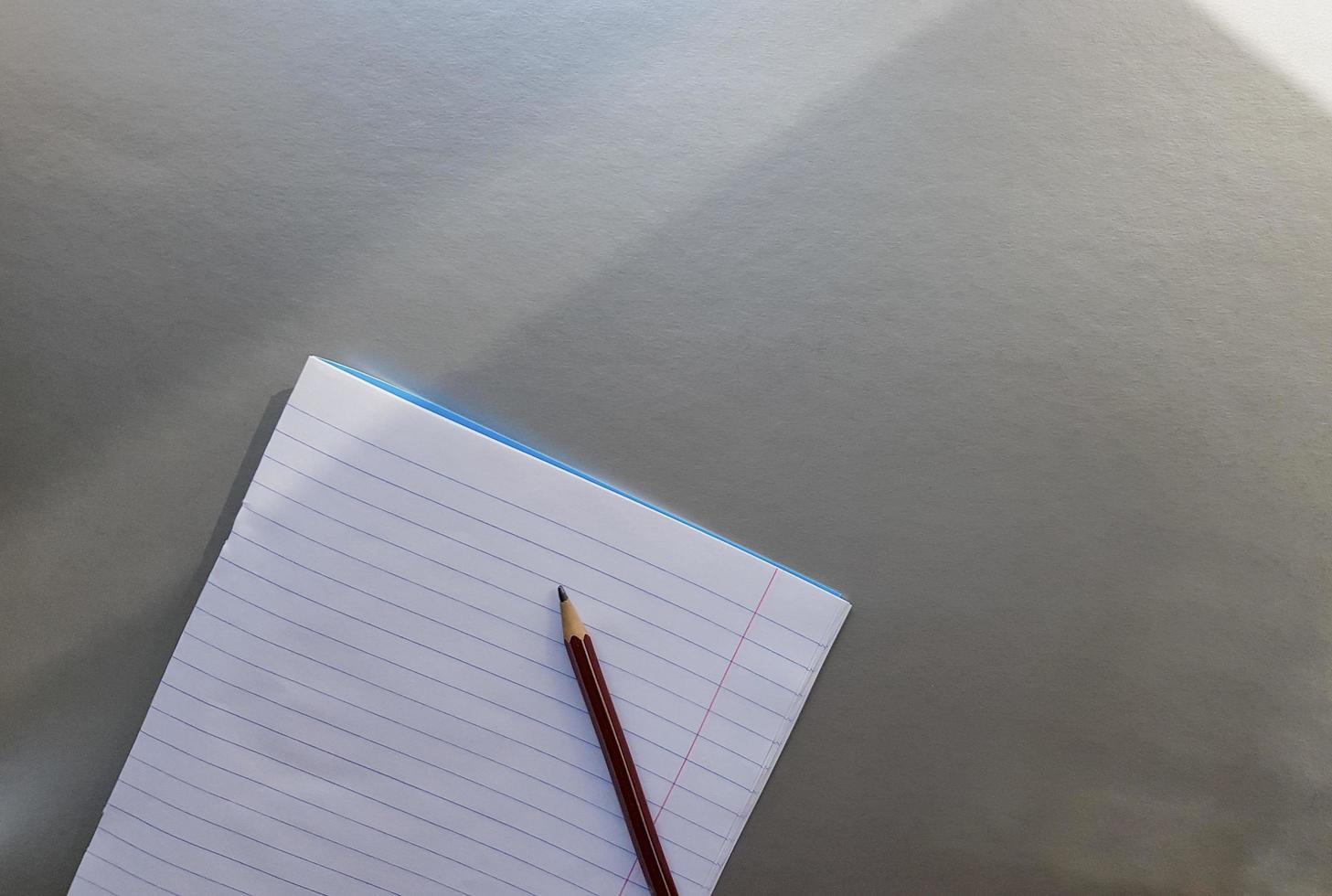 cuaderno escolar abierto con bolígrafo sobre un escritorio gris con rayos de sol desde la ventana. una hoja de cuaderno en blanco para escribir. concepto de educación. copie el espacio. vista desde arriba. endecha plana foto