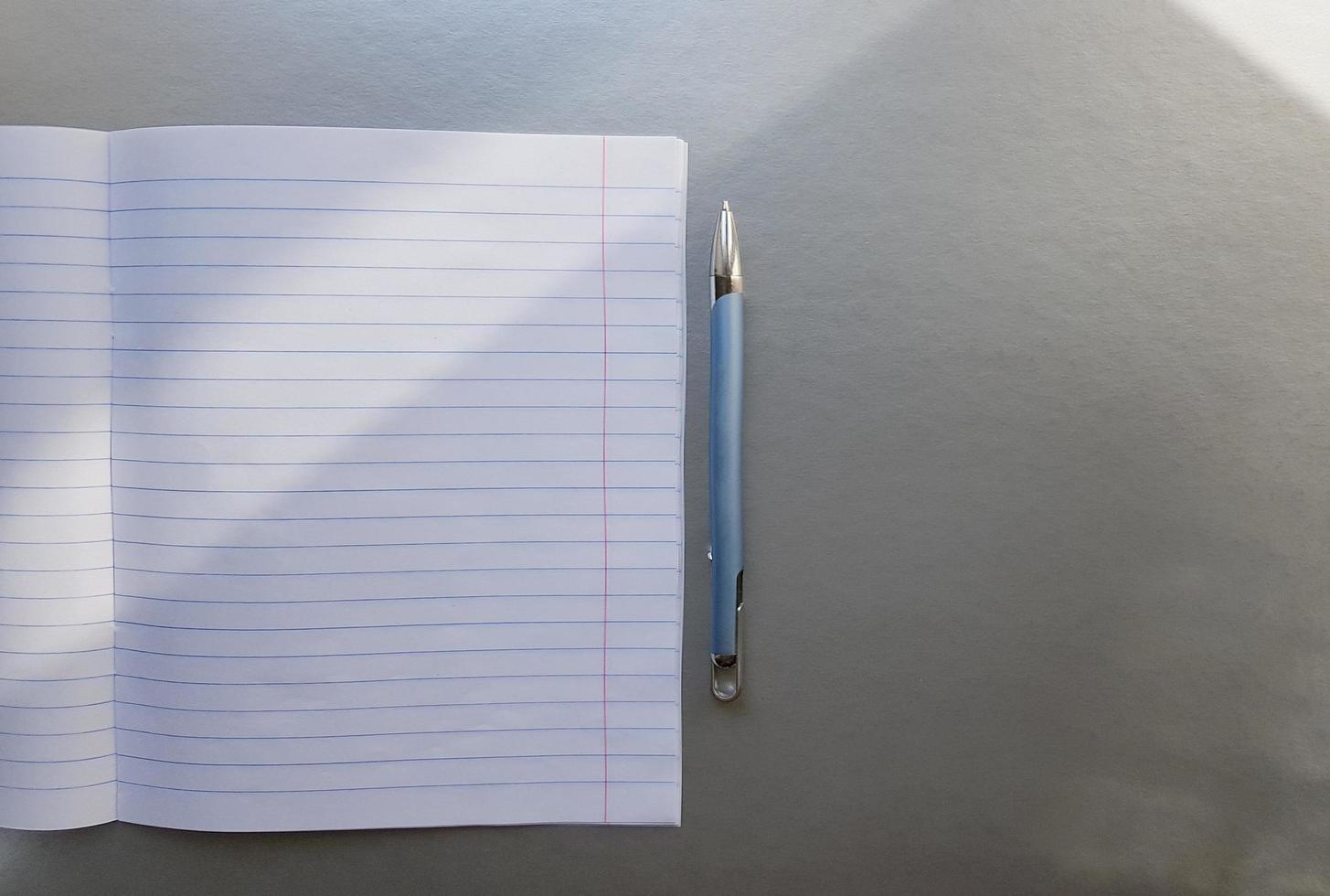 cuaderno escolar abierto con bolígrafo sobre un escritorio gris con rayos de sol desde la ventana. una hoja de cuaderno en blanco para escribir. concepto de educación. copie el espacio. vista desde arriba. endecha plana foto