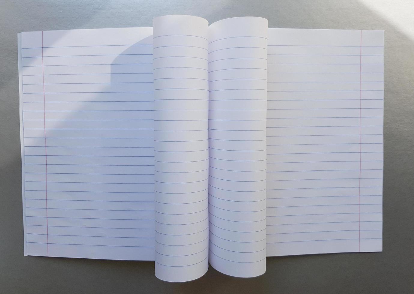 open school notebook with pen on a gray desk with sun rays from the window. A blank, white sheet of notebook for writing. education concept. Copy space. view from above. Flat lay photo