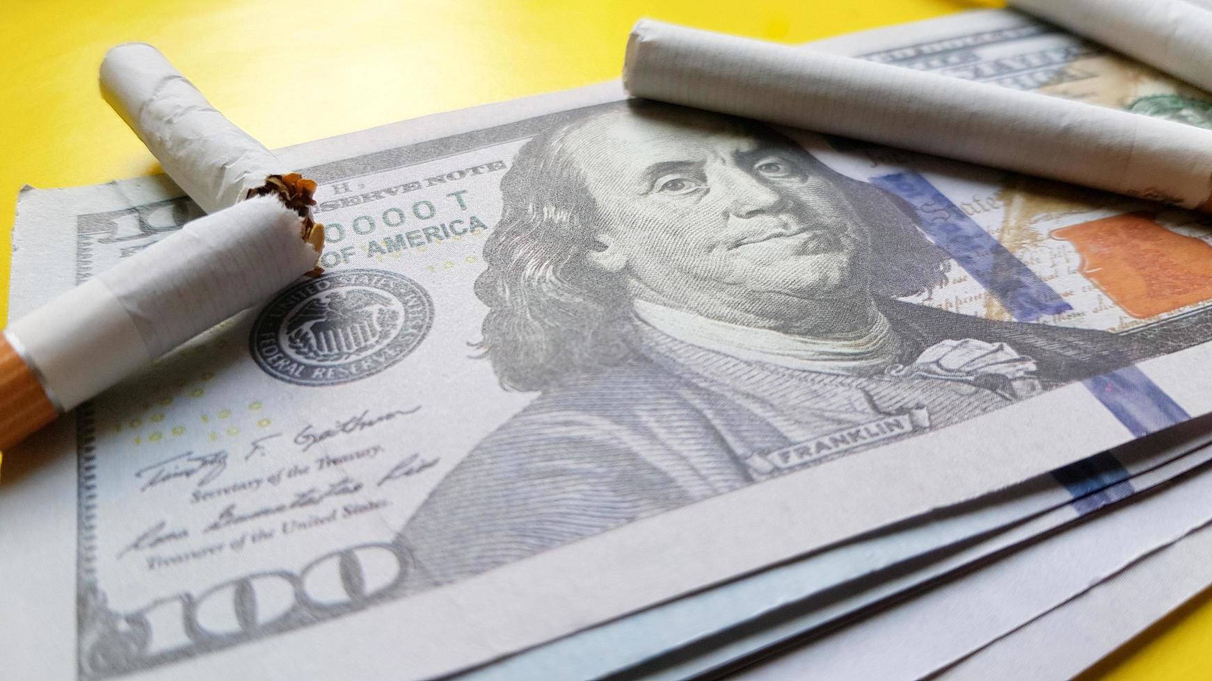 Classic cigarettes stand on one hundred US dollar bills. Cigarettes on a hundred dollar bill on a yellow background photo