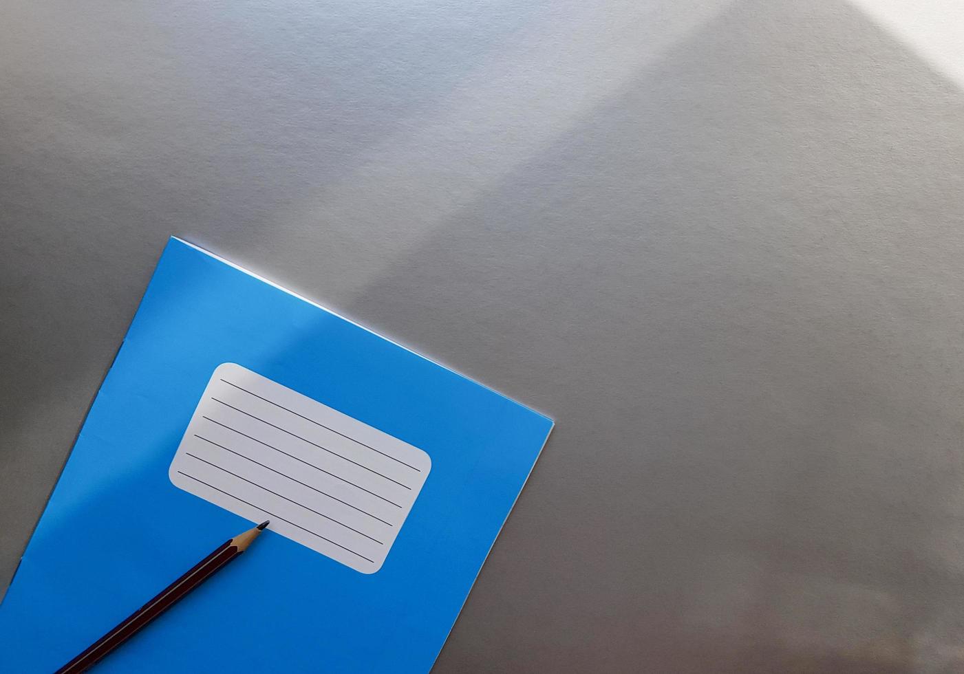 New blue notebook with pencil on a gray table with sun rays from the window background photo