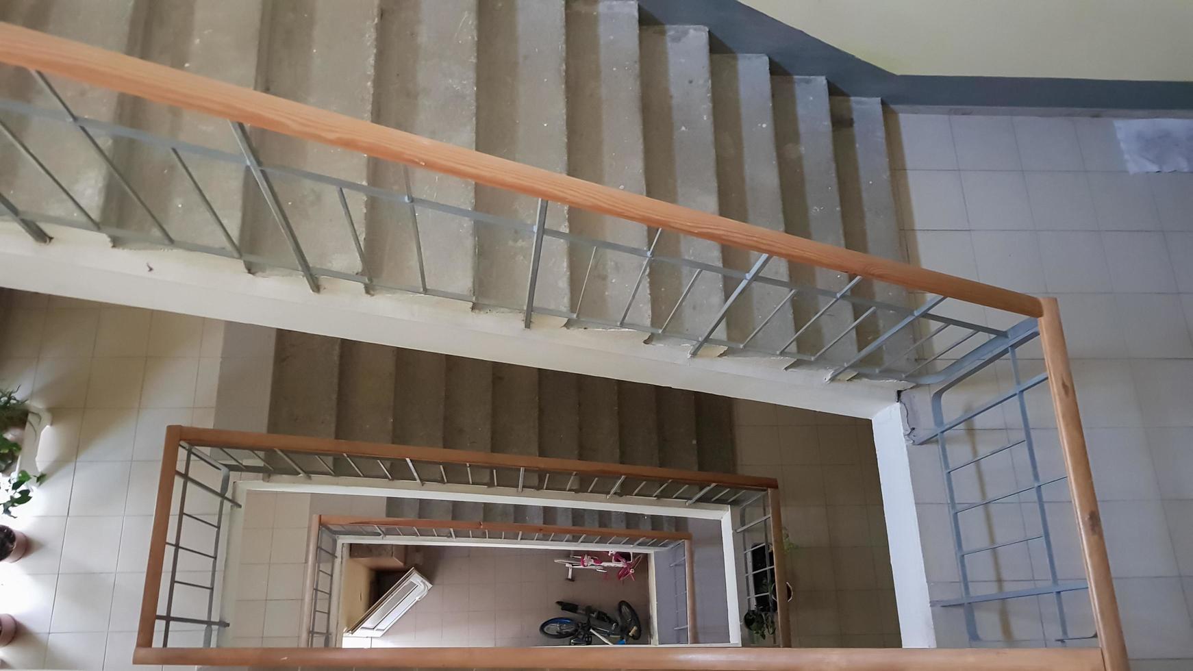 Modern stairwell in a residential building. Staircase in perspective. Gray ceramic tile. Common staircase with a brown wooden fence and concrete steps. View from above. photo