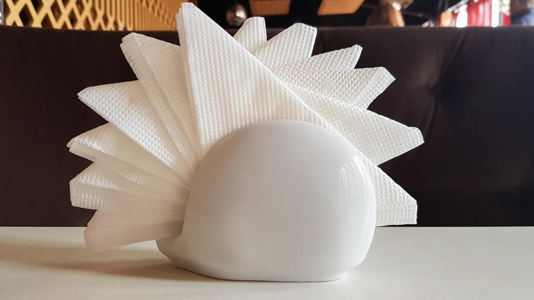 A table in a cafe and restaurant. White napkins in a ceramic napkin holder. Hotel dining table with napkins. A paper napkin is placed in a glass on a table in the banquet room. photo