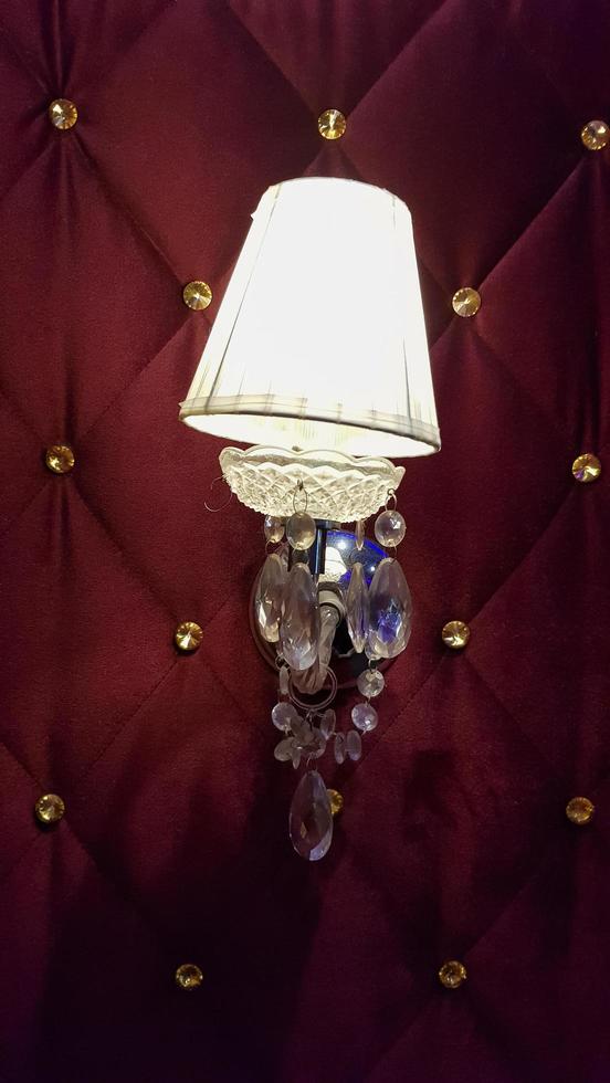 Retro bedroom lamp with a red wall. Antique sconces hanging on a wall of textile with buttons. photo