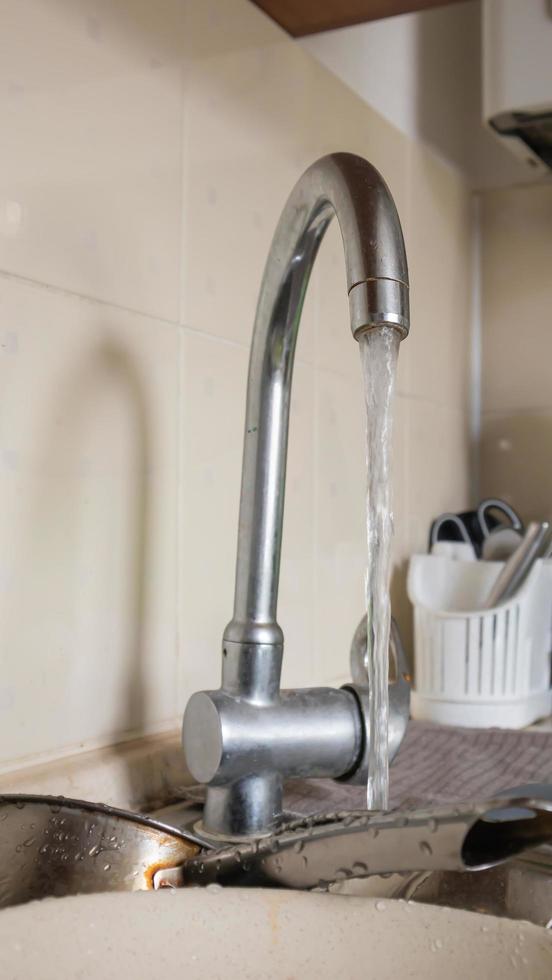 The kitchen utensils in the wash basin need to be washed. A pile of dirty dishes in the kitchen sink with running water. Kitchen utensils need washing. Homework concept. photo