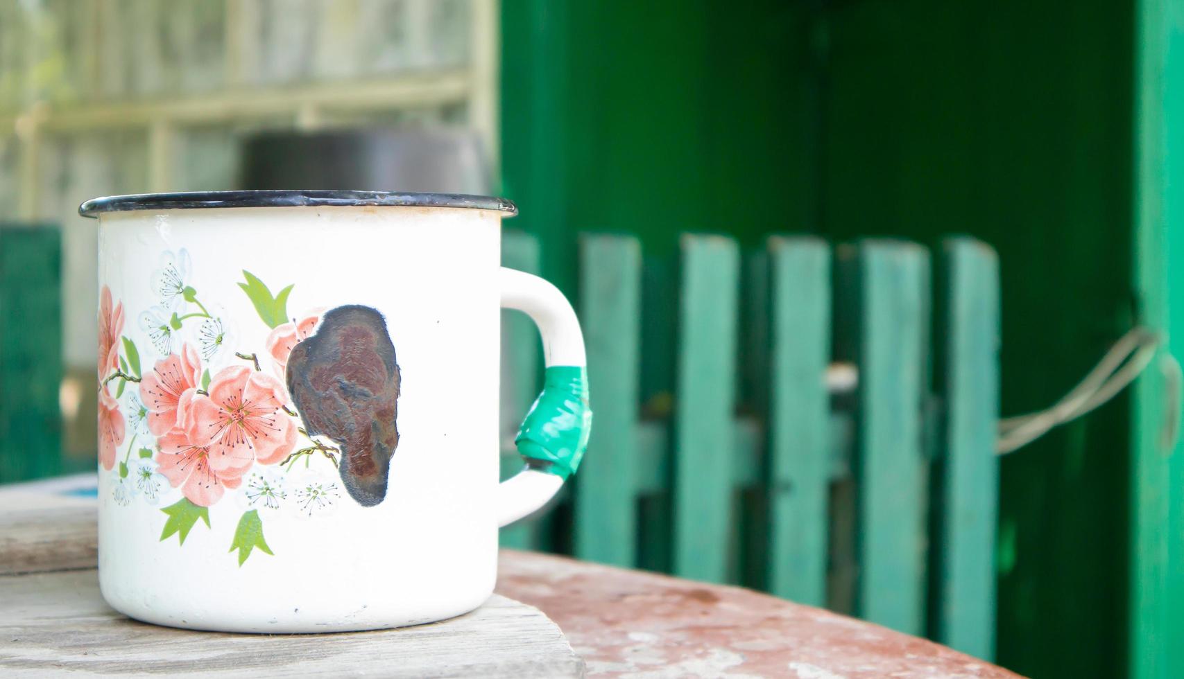 Vintage enamel mug. An old large metal mug in the village on the well. Empty dishes in the courtyard of a rural house as a traditional thing in the villages. photo