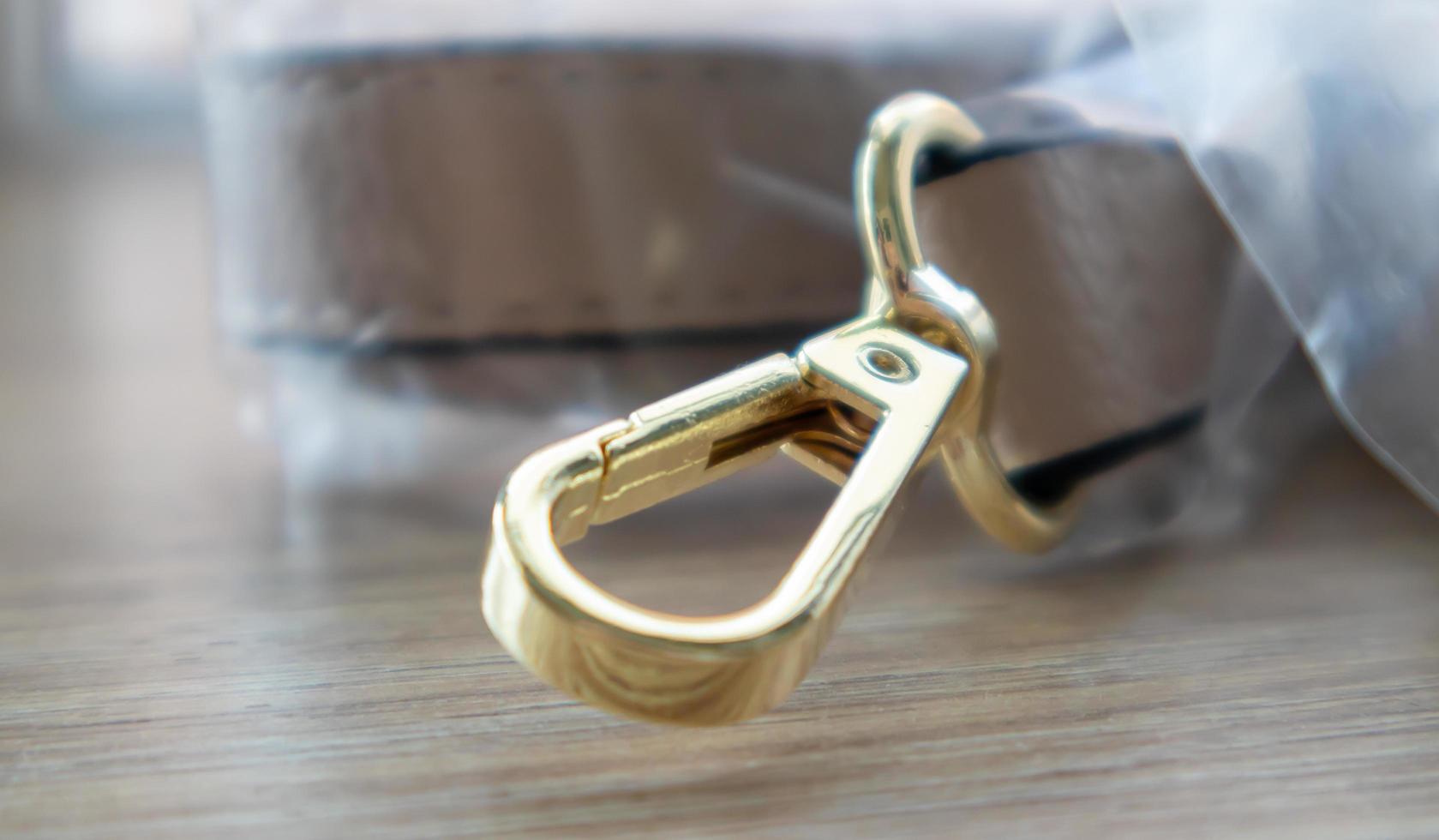 Swivel snap fastener with leather beige bag strap on a wooden background. Metal carabiner with swivel clip or hook. Small gold fittings close-up in selective focus. photo
