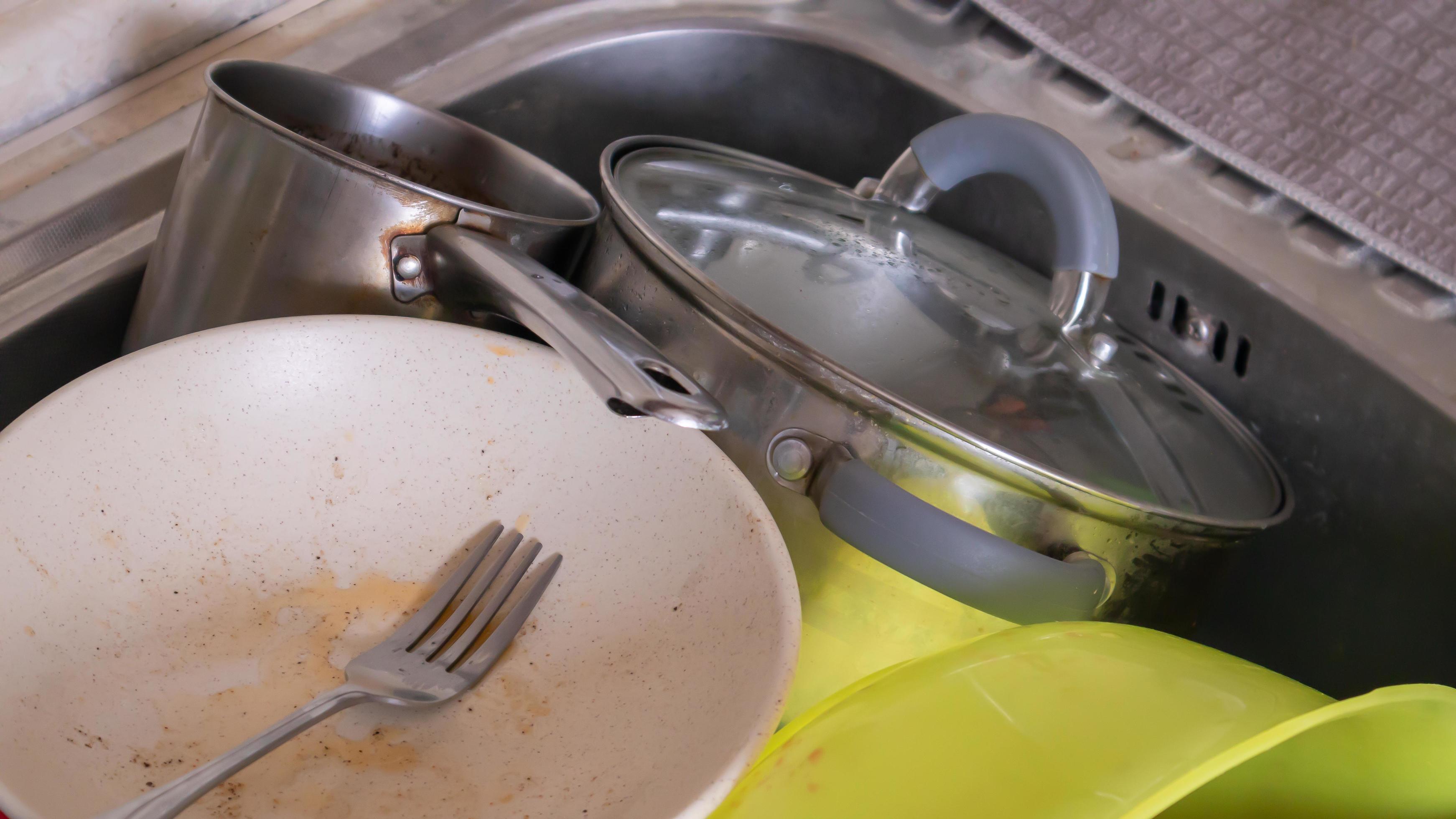 The kitchen utensils in the wash basin need to be washed. A pile of dirty dishes in the kitchen