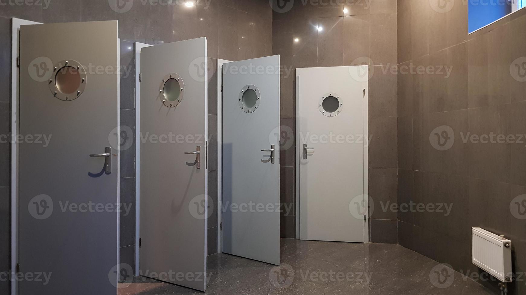 The public building has female and male toilets with four gray doors. Terrier with gray tiles on the walls and floor. photo
