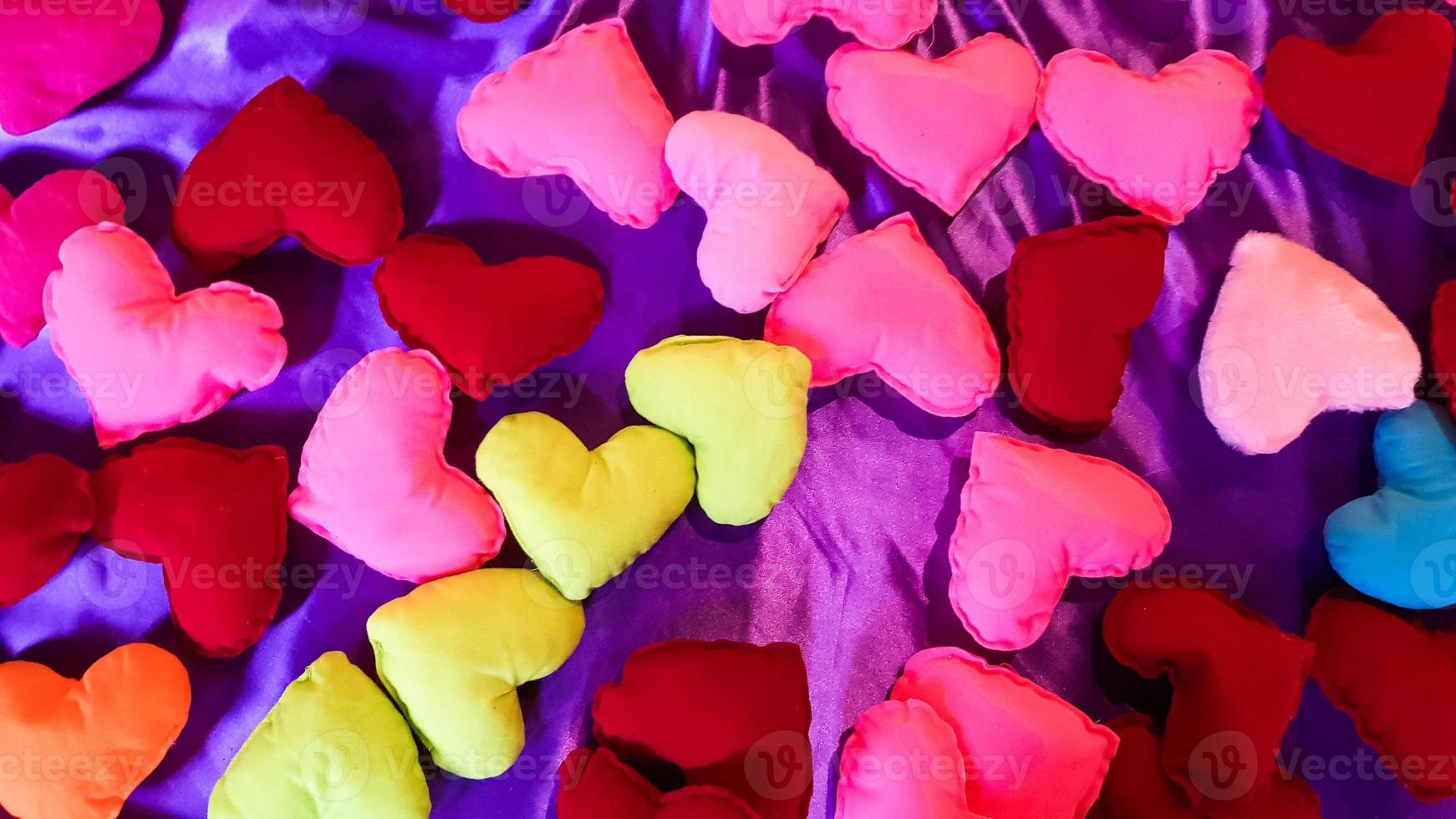 Corazones de felpa multicolores y brillantes sobre un fondo de cama morado. día de san valentín o concepto de amor. foto