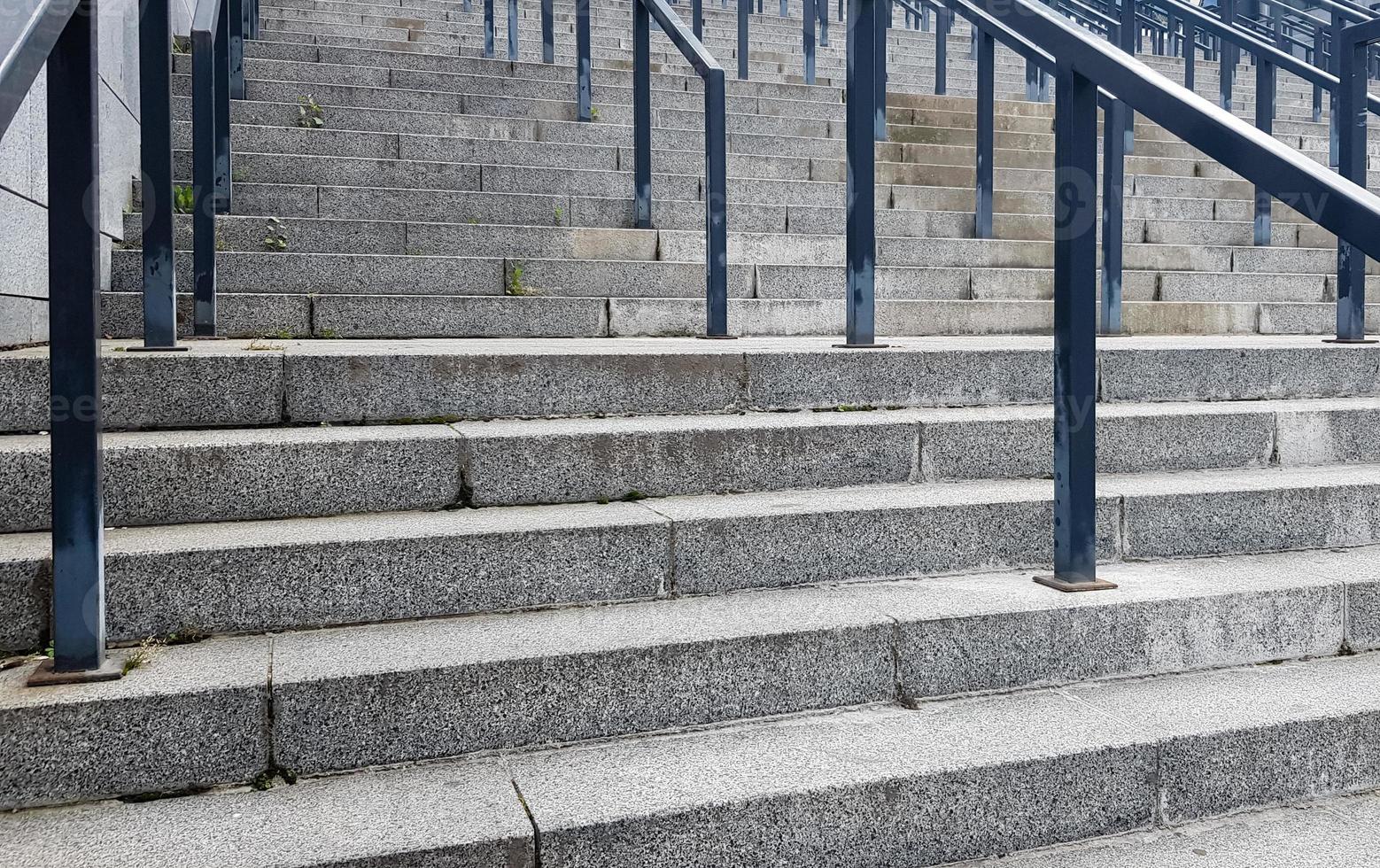 External multi-stage stone staircase. There are a lot of stairs and railings made of metal. Many steps in an urban environment, symbolic abstract background. photo